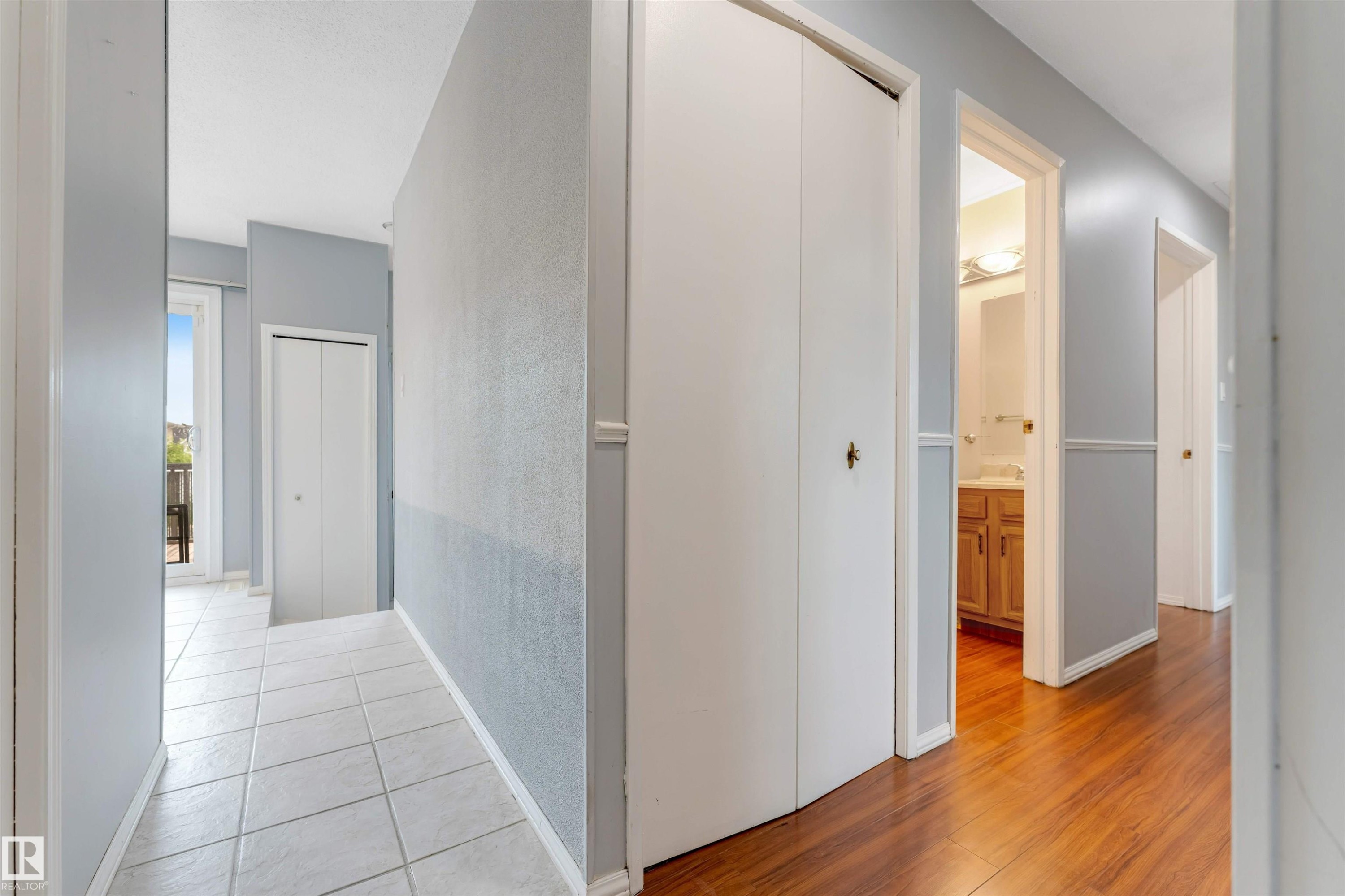 Hallway featuring light blue walls with wainscoting, wood-finish flooring, white bi-fold closet doors, and white trim - 193 Woodvale Road W, Edmonton, AB