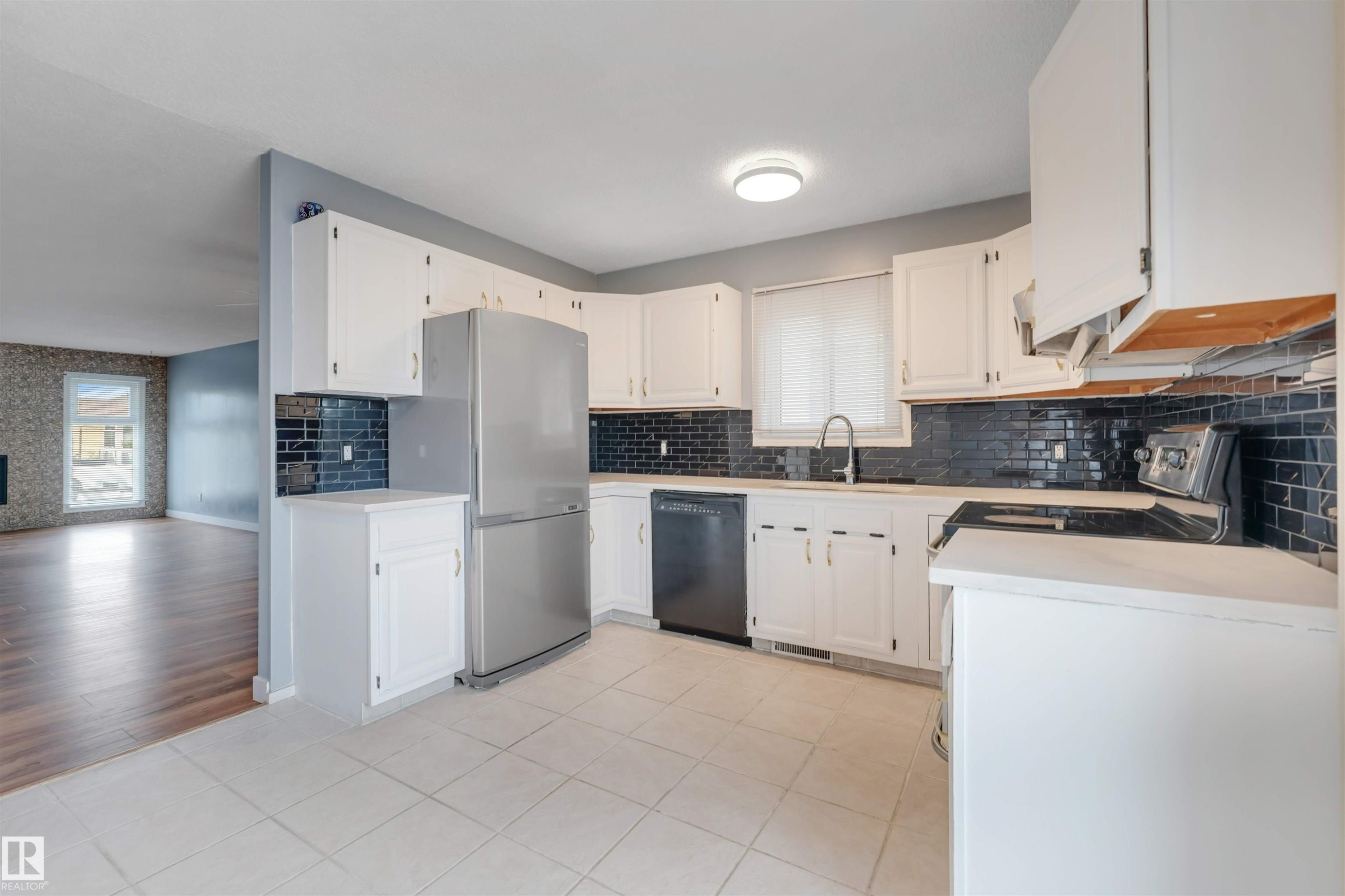 Kitchen featuring white cabinetry, black subway tile backsplash, stainless steel refrigerator, black dishwasher, and white tile flooring - 193 Woodvale Road W, Edmonton, AB