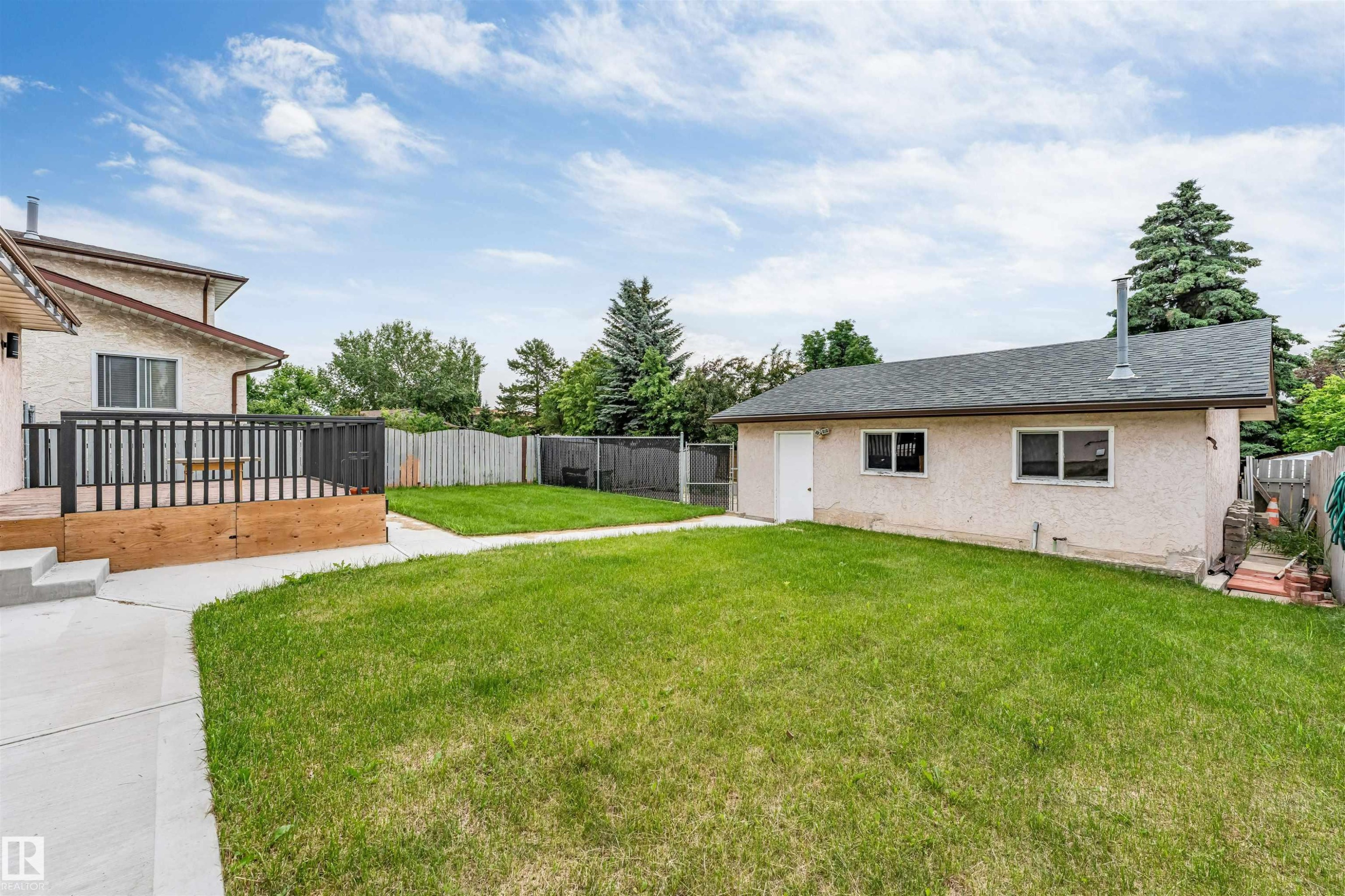 Expansive backyard featuring a manicured lawn, concrete pathway, and a large wood deck with dark railings - 193 Woodvale Road W, Edmonton, AB
