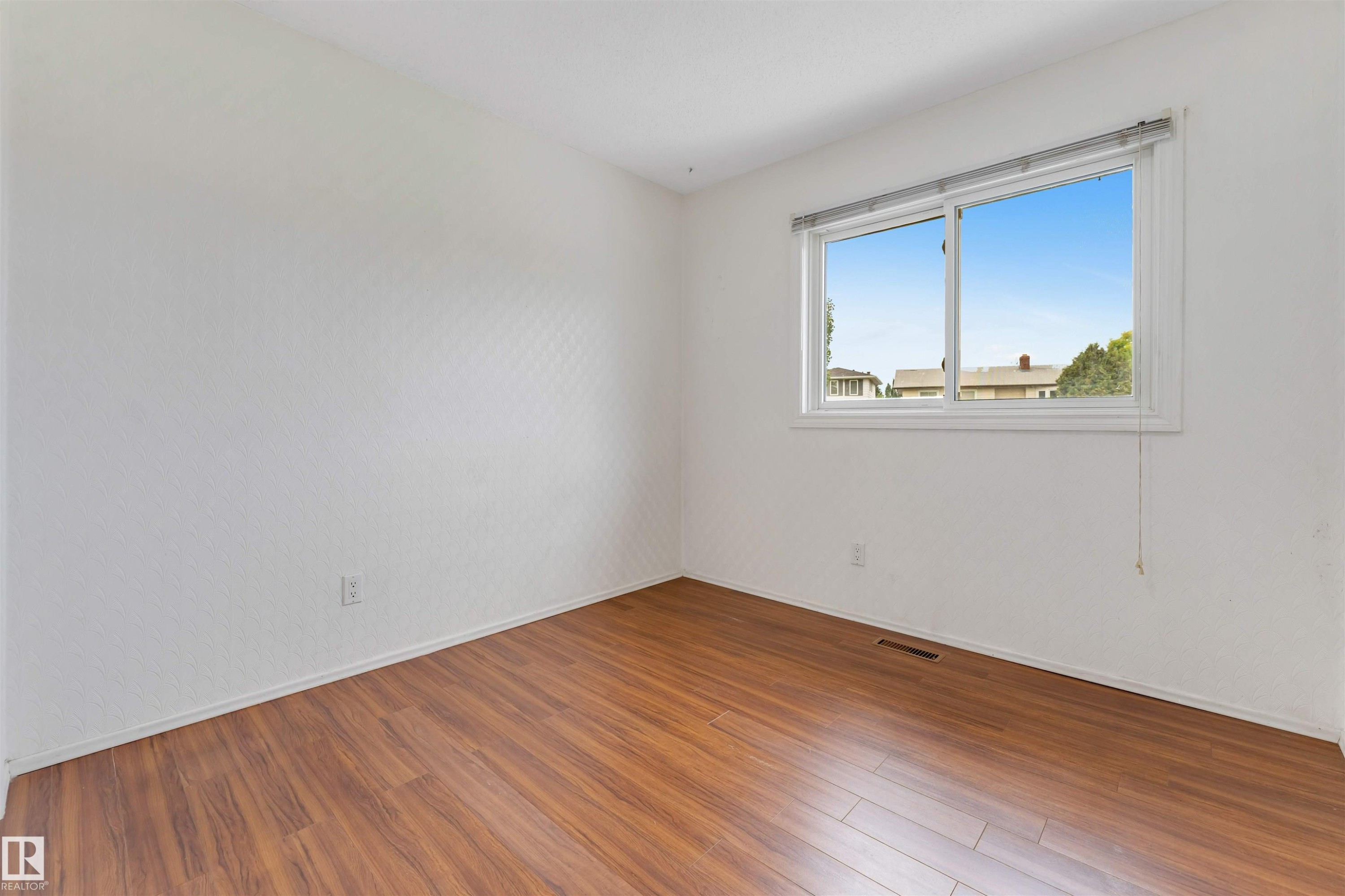 Room featuring a large window, wood-finish flooring, white baseboards, and neutral wall tones - 193 Woodvale Road W, Edmonton, AB