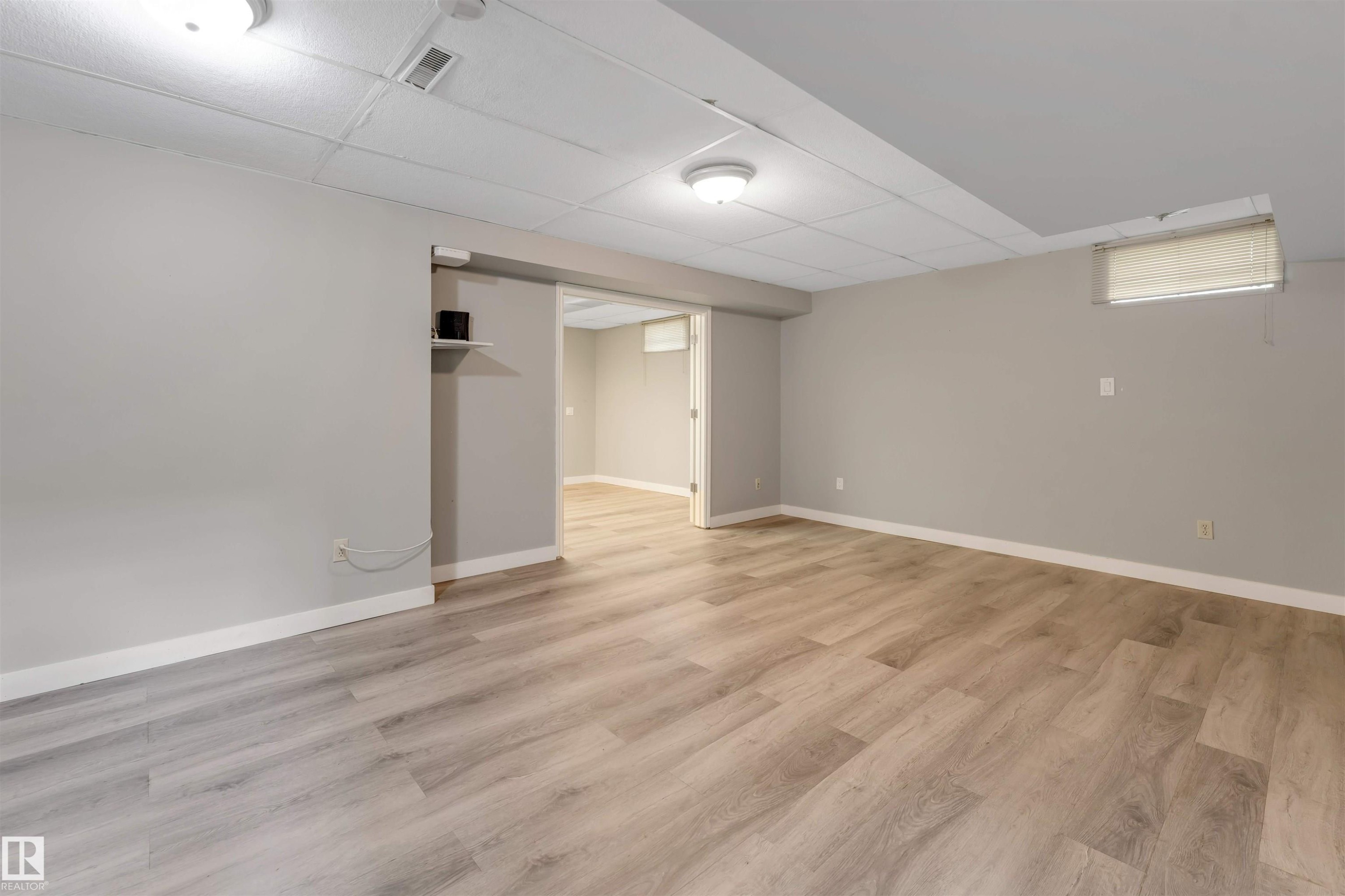 Spacious room featuring light wood-finish flooring, neutral wall tones, white baseboards, and a suspended acoustic ceiling - 193 Woodvale Road W, Edmonton, AB
