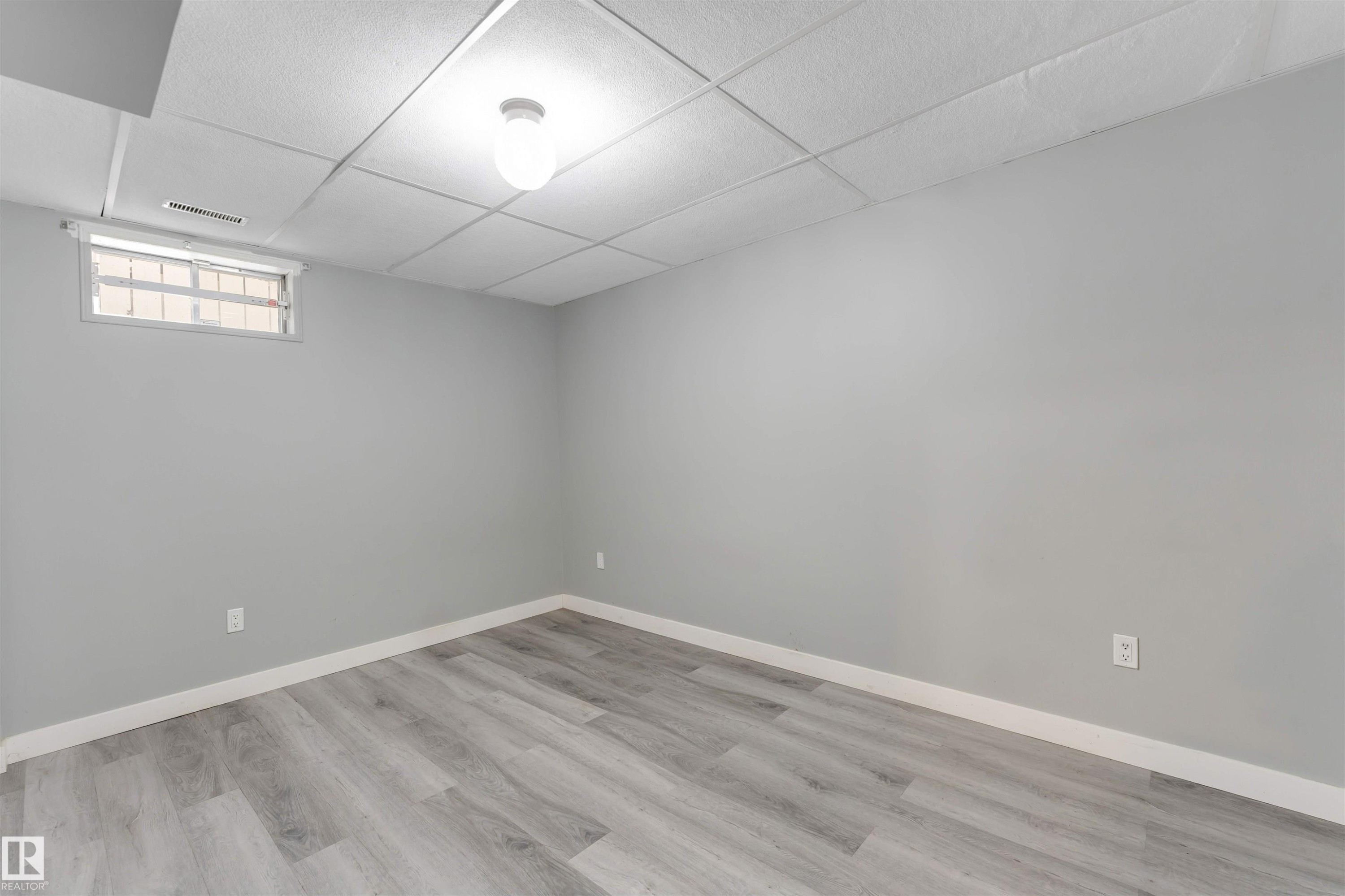Spacious interior room featuring light gray walls, wood-finish flooring, a drop ceiling with recessed lighting, and a horizontal window with white trim - 193 Woodvale Road W, Edmonton, AB