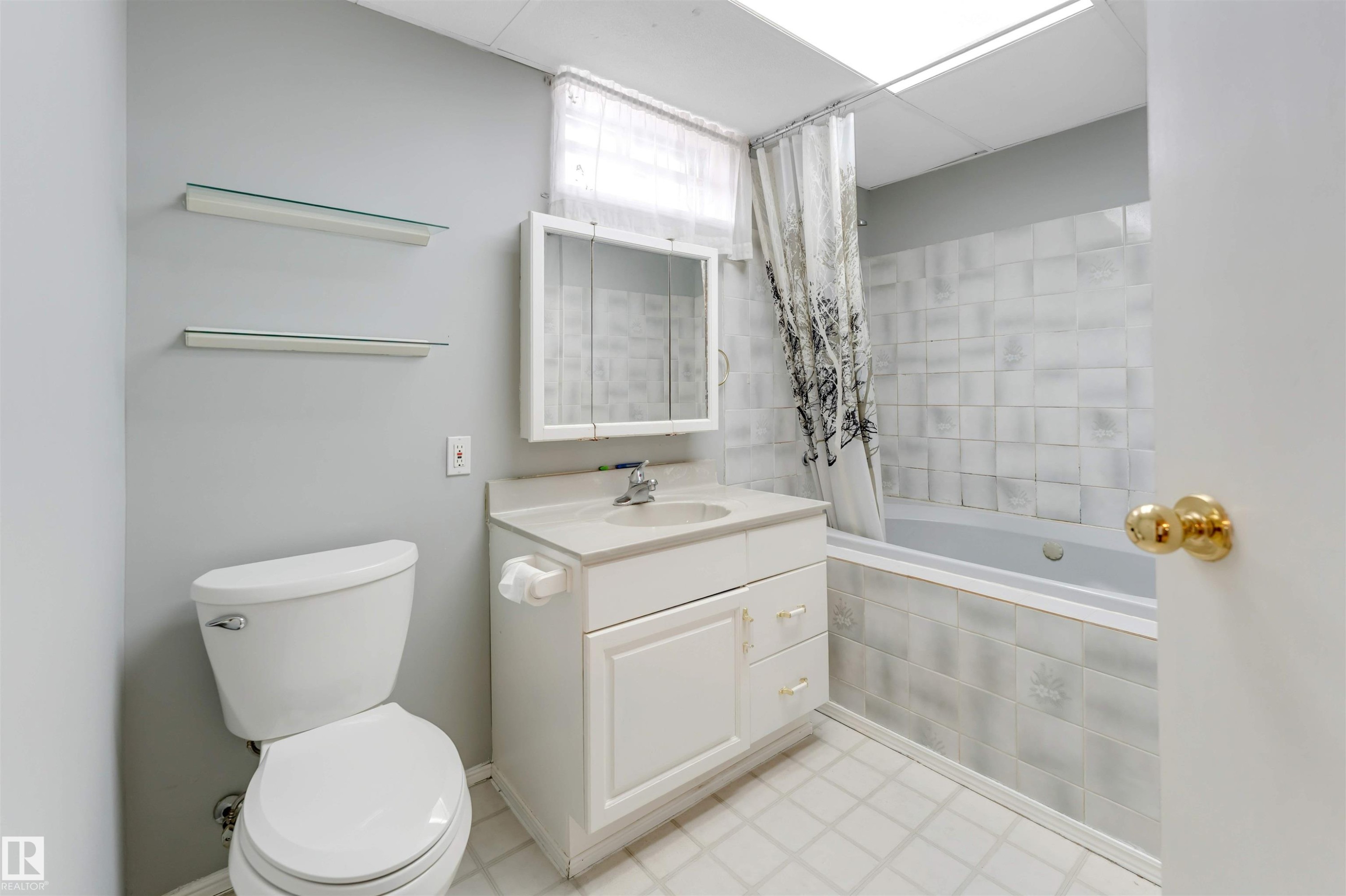 Full bathroom featuring a white vanity with integrated sink, coordinating toilet, and a tiled tub surround - 193 Woodvale Road W, Edmonton, AB