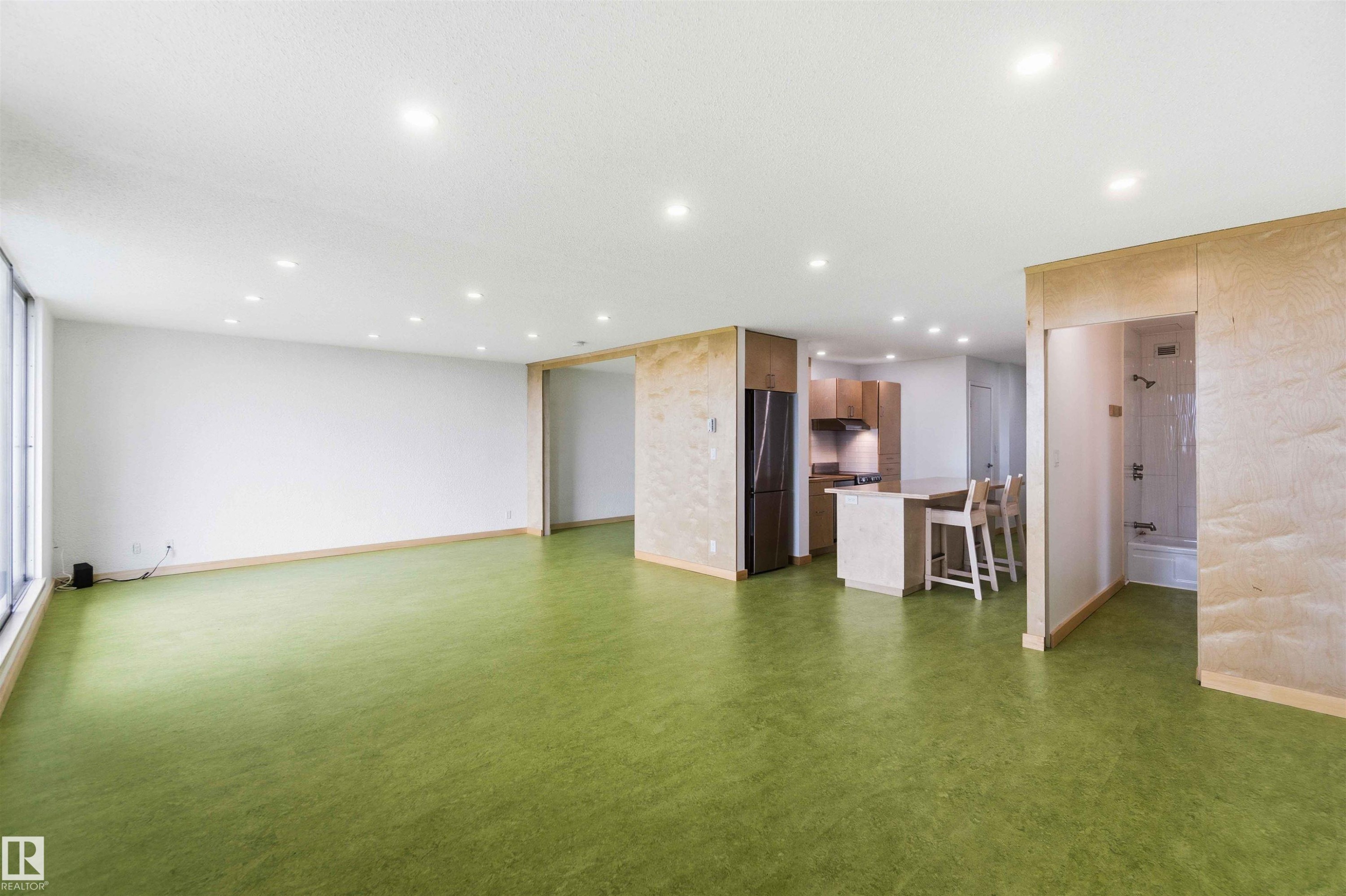 Spacious interior featuring a large window, recessed lighting, and green-hued flooring - #1008 11307 99 Av Nw, Edmonton, AB