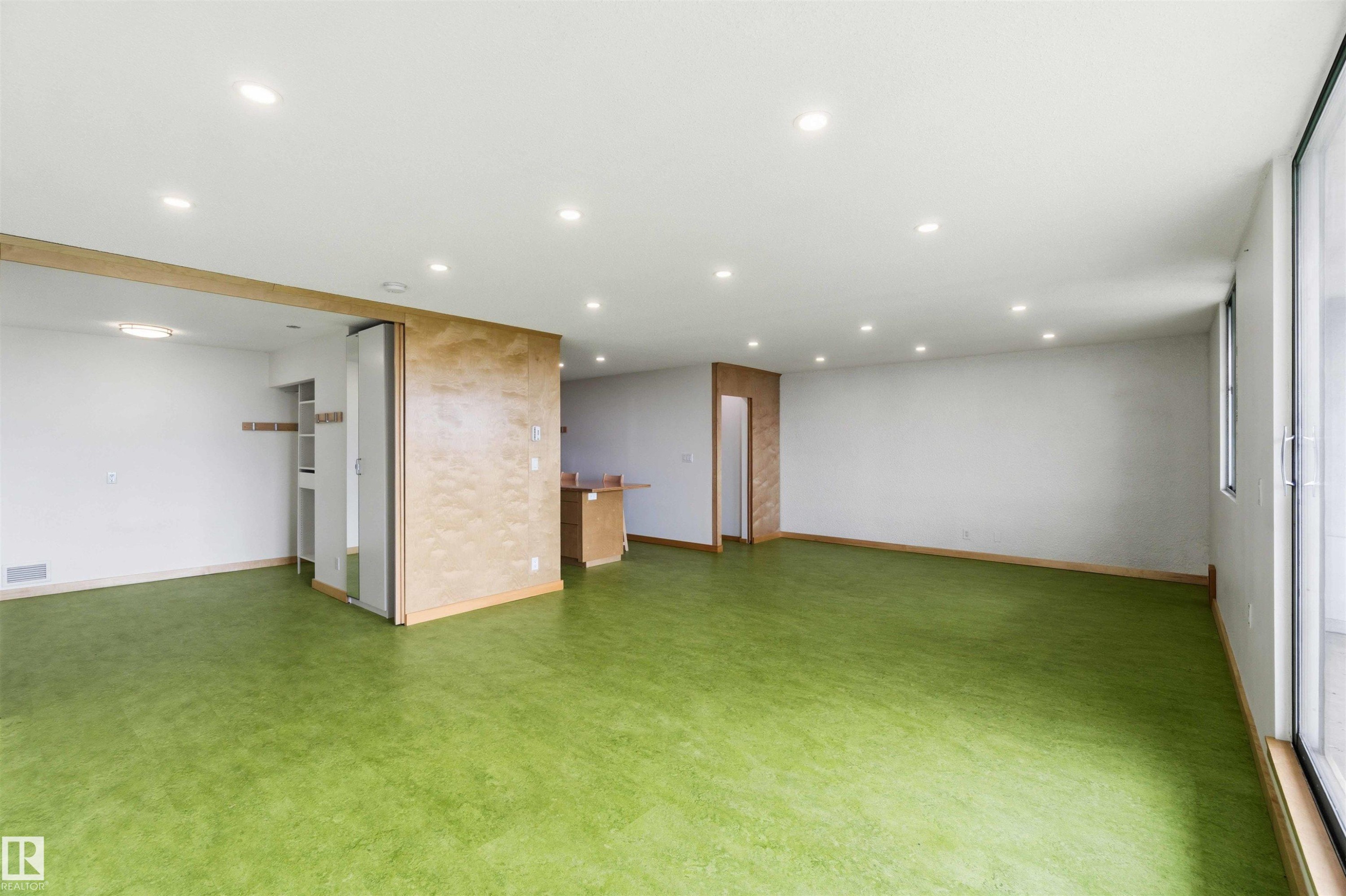 Spacious room featuring green flooring, recessed lighting, and a sliding glass door - #1008 11307 99 Av Nw, Edmonton, AB