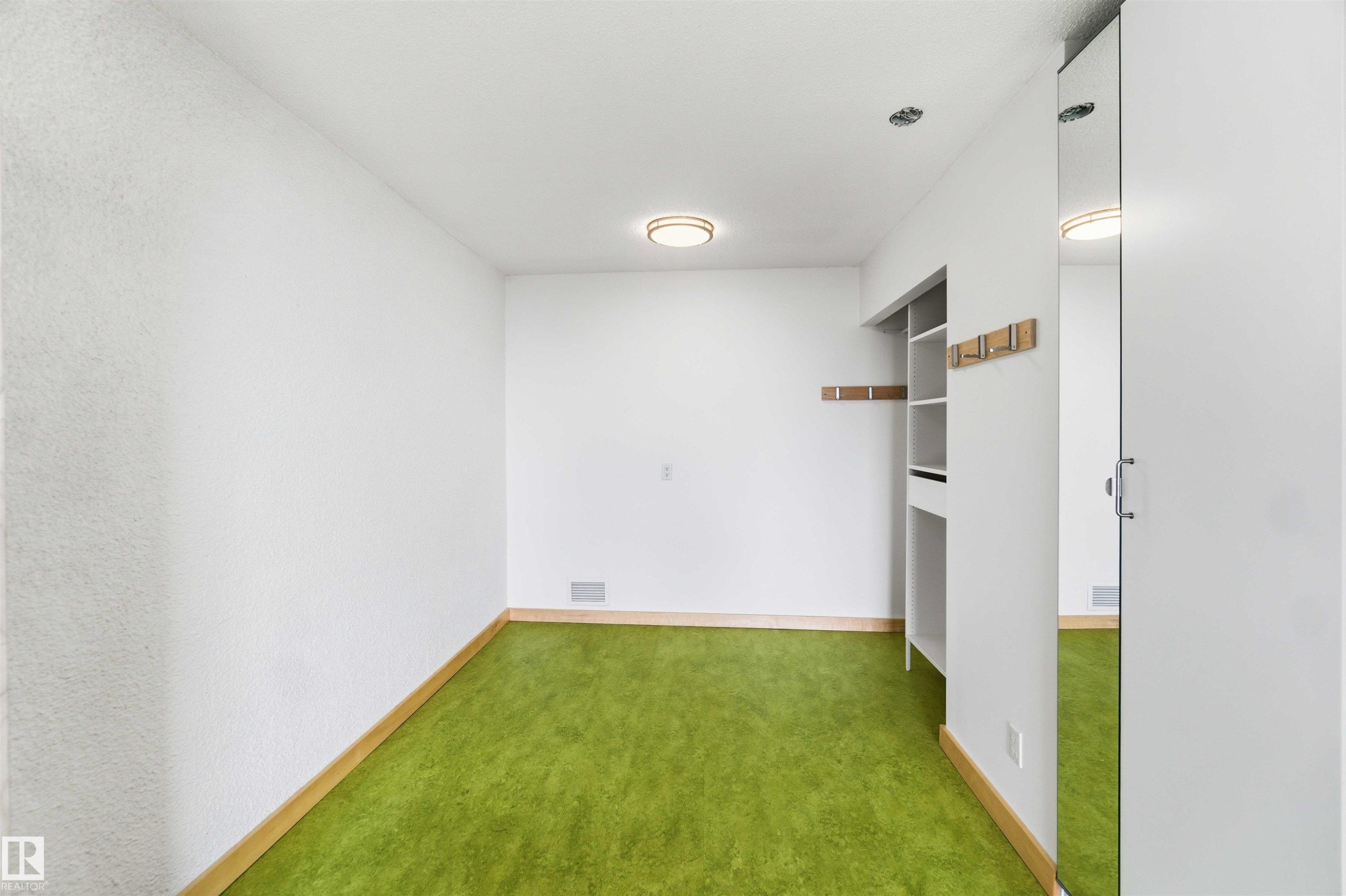 Room featuring green carpet flooring, white walls, and a built-in closet system with open shelving - #1008 11307 99 Av Nw, Edmonton, AB