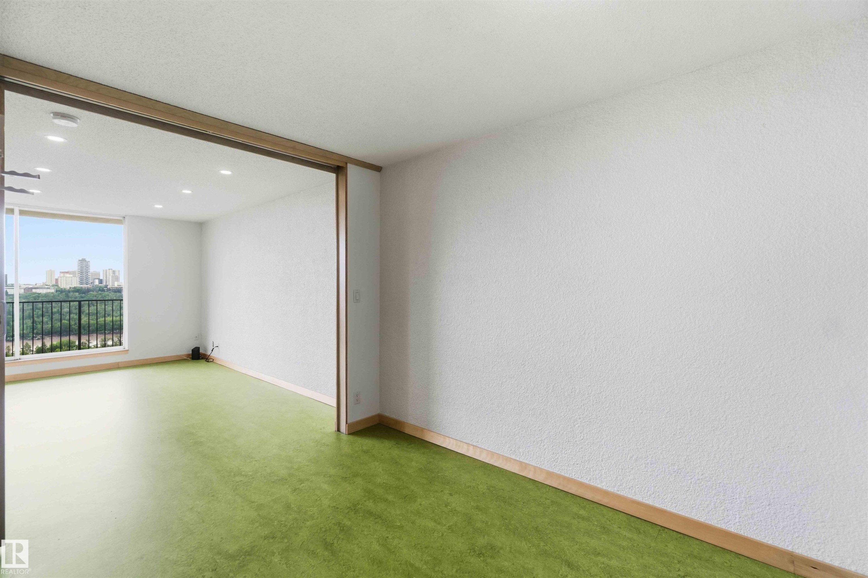 Expansive interior space featuring a full-height window, green flooring, recessed ceiling lighting, and a cityscape backdrop - #1008 11307 99 Av Nw, Edmonton, AB
