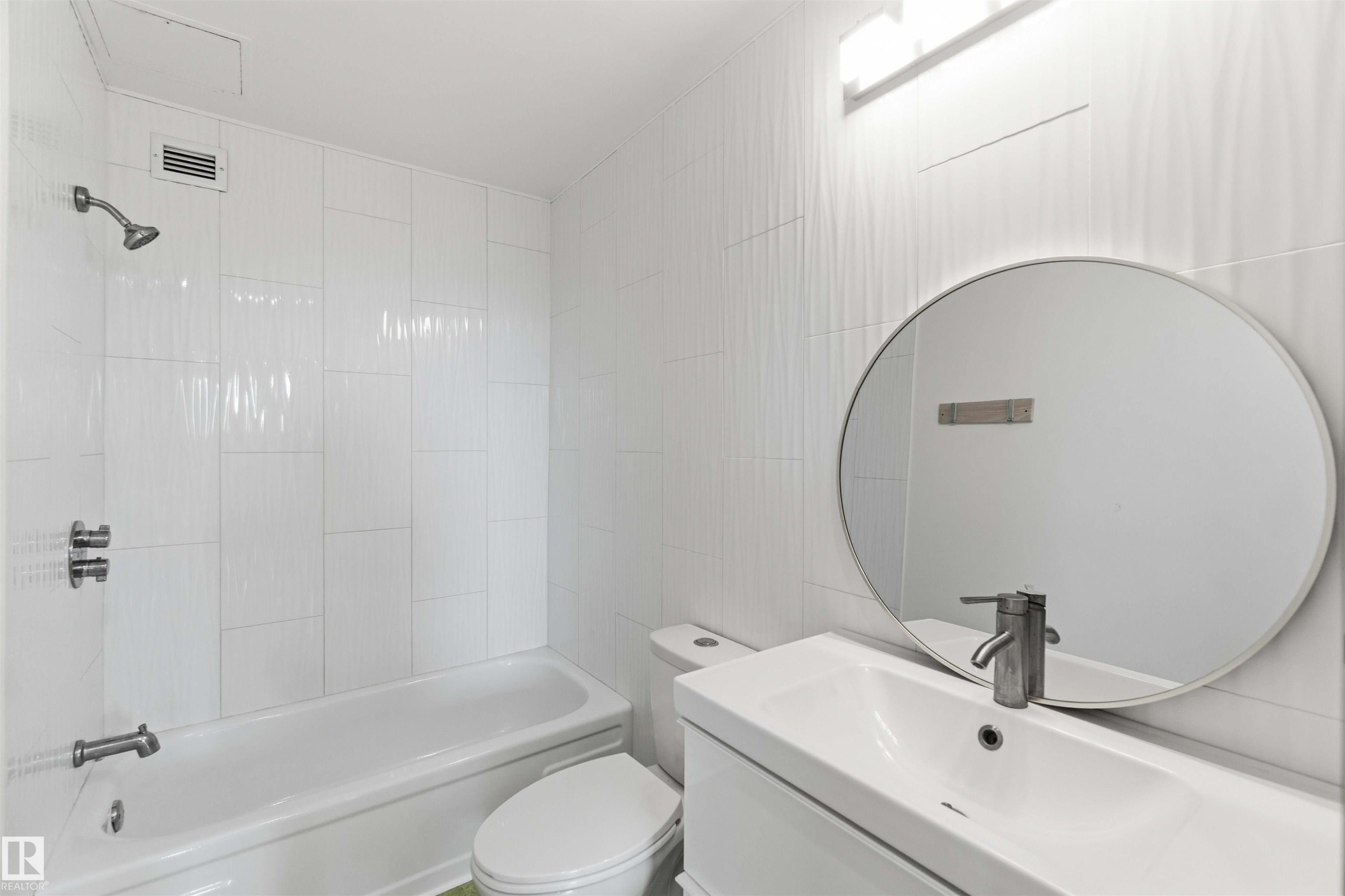 Bathroom featuring a white vanity with integrated sink, brushed nickel faucet, and circular mirror - #1008 11307 99 Av Nw, Edmonton, AB