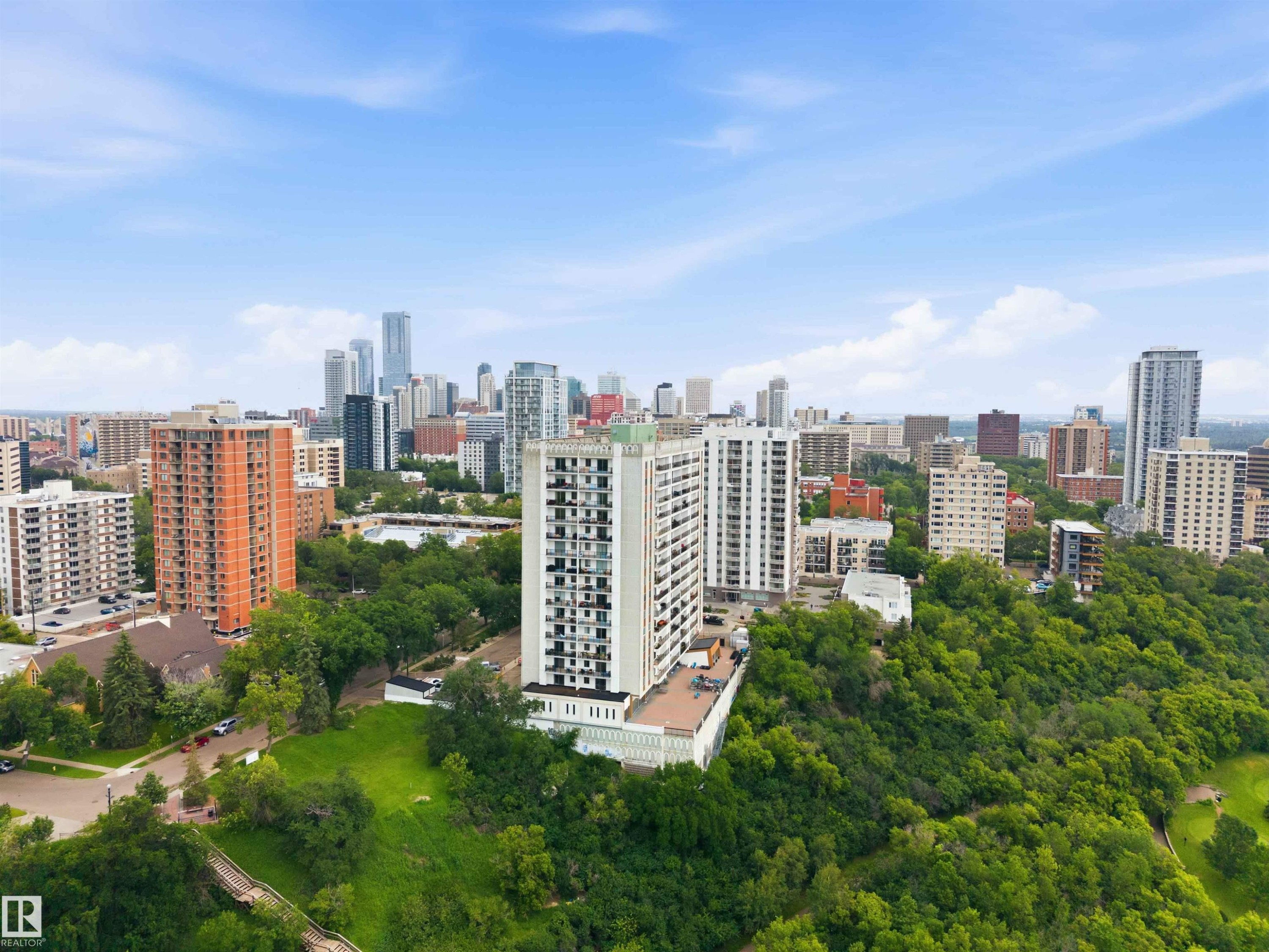 High-rise building with a tiered base, surrounded by abundant mature trees and a cityscape backdrop - #1008 11307 99 Av Nw, Edmonton, AB