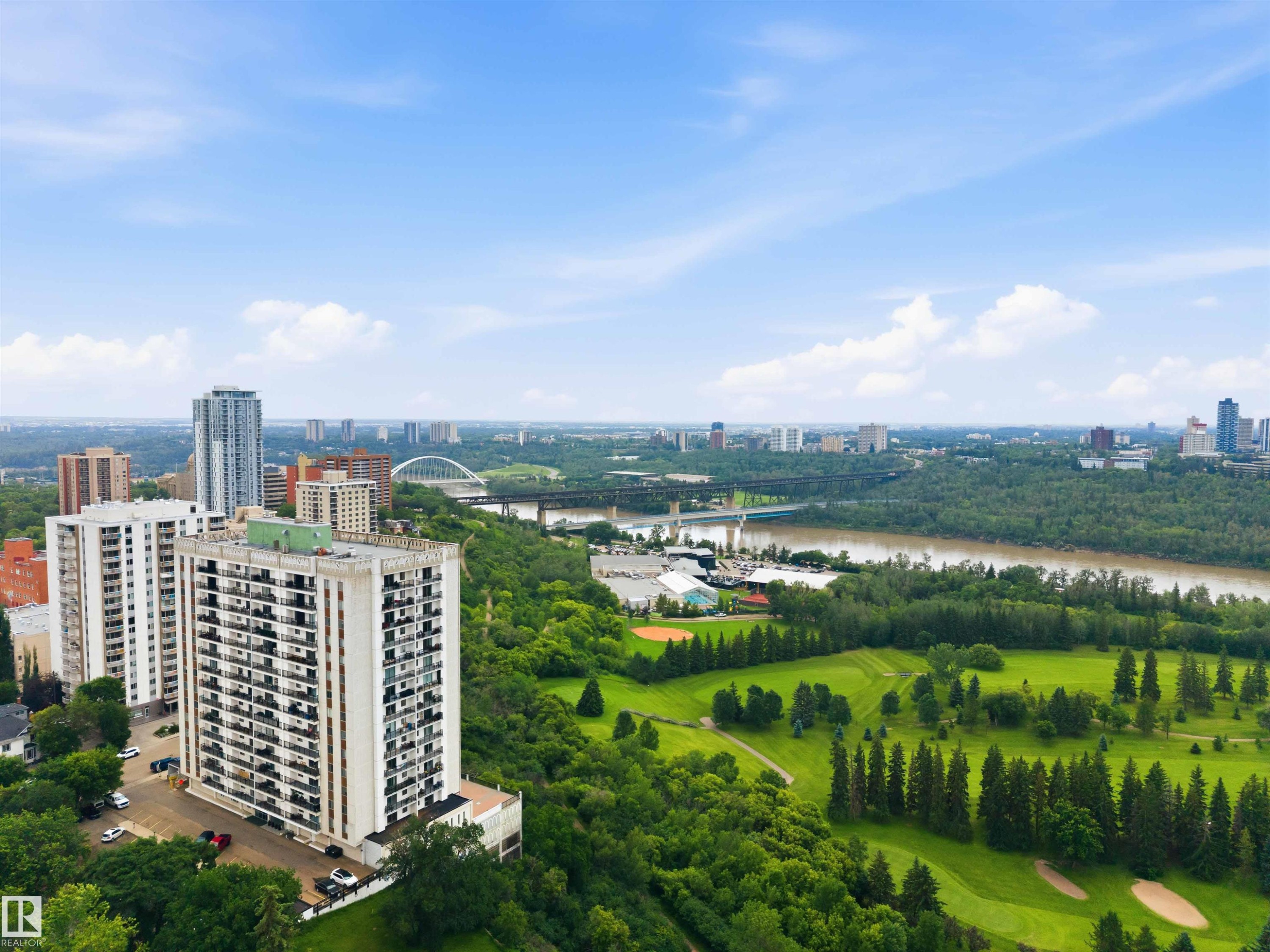Elevated residential building with multiple balconies overlooking a river, golf course, and urban skyline - #1008 11307 99 Av Nw, Edmonton, AB