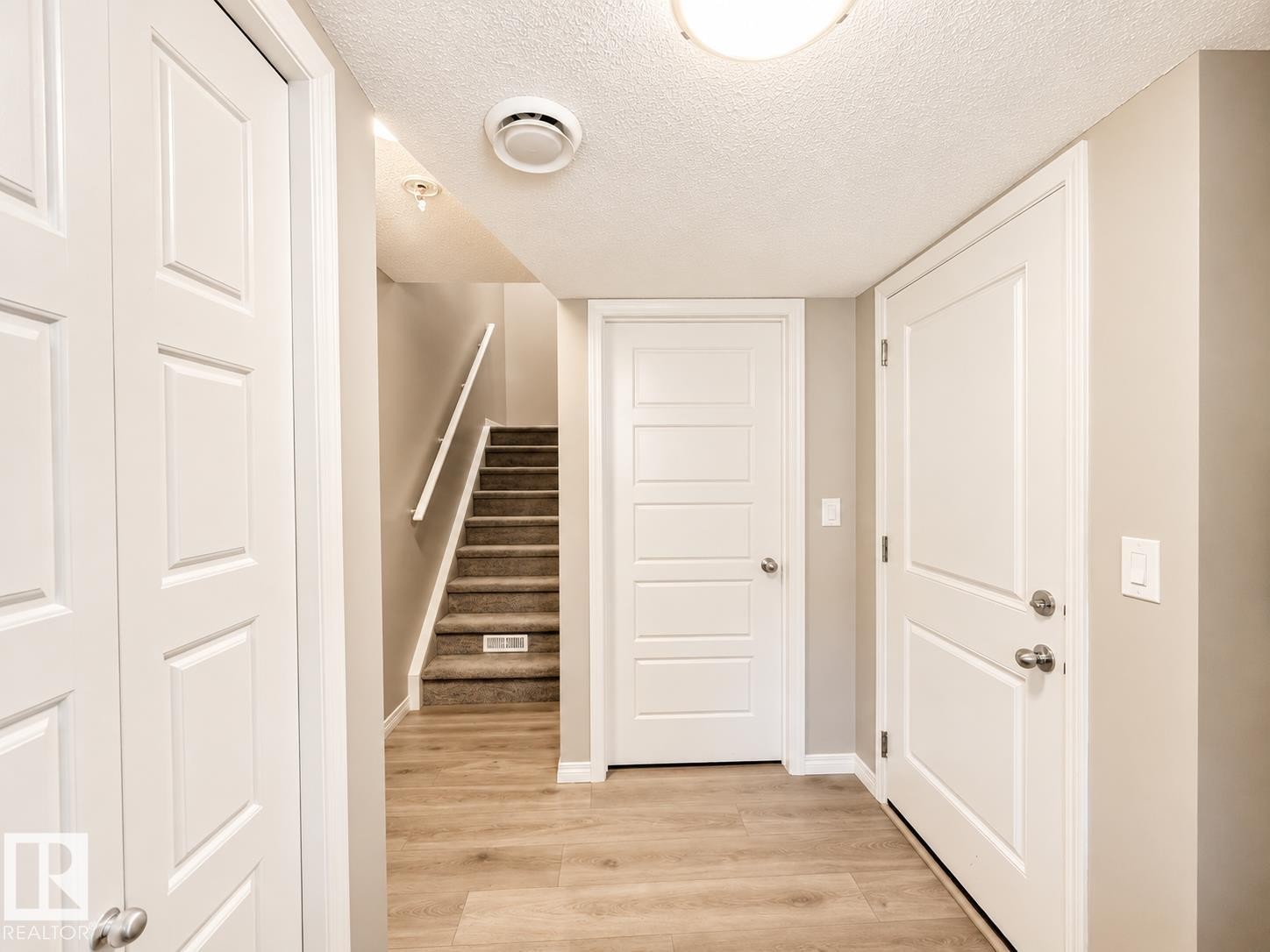 Light wood-finish flooring extending from the entryway to a carpeted staircase with a white handrail - 20104 19 Avenue, Edmonton, AB