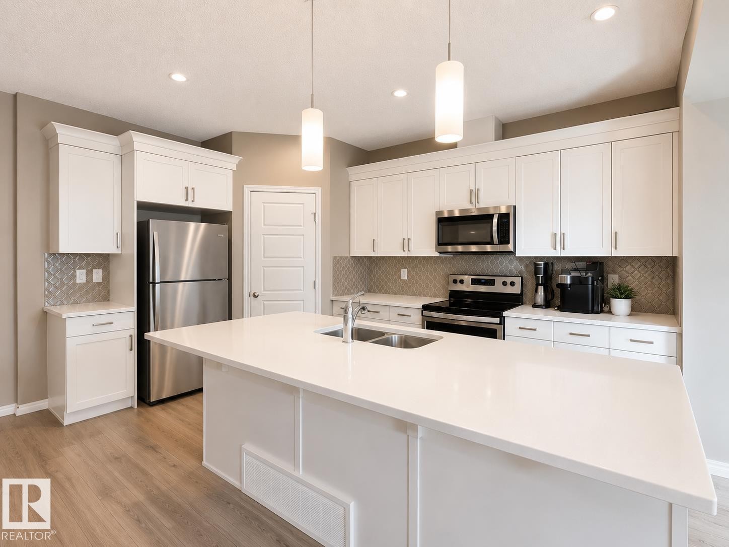 Kitchen featuring a large central island with a double sink, white cabinetry with crown molding, stainless steel appliances, and a decorative tile backsplash - 20104 19 Avenue, Edmonton, AB