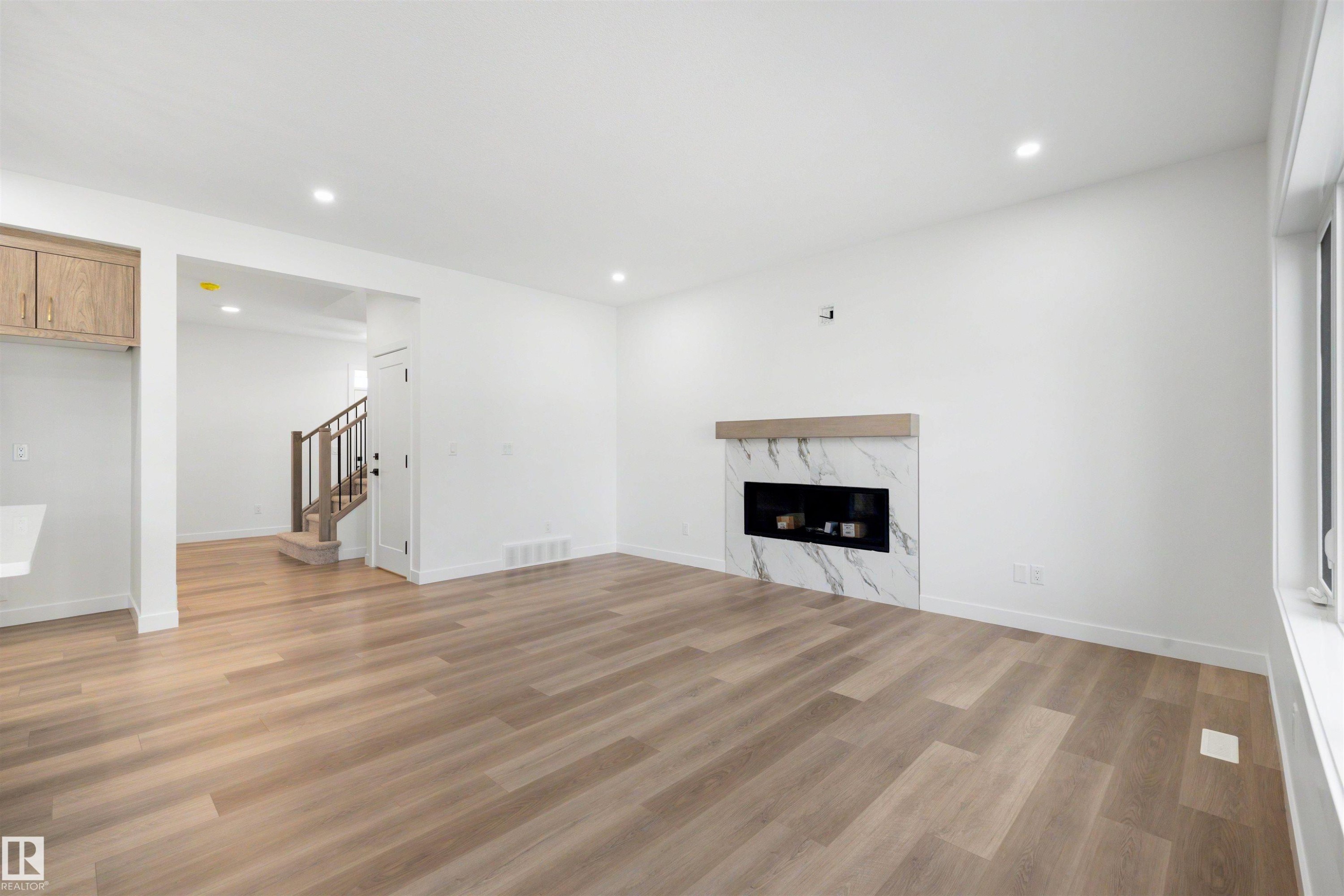Living space featuring wood-finish flooring, recessed lighting, and a modern fireplace with a marble-look surround and wood mantel - 30 Elsinore Place Nw, Edmonton, AB