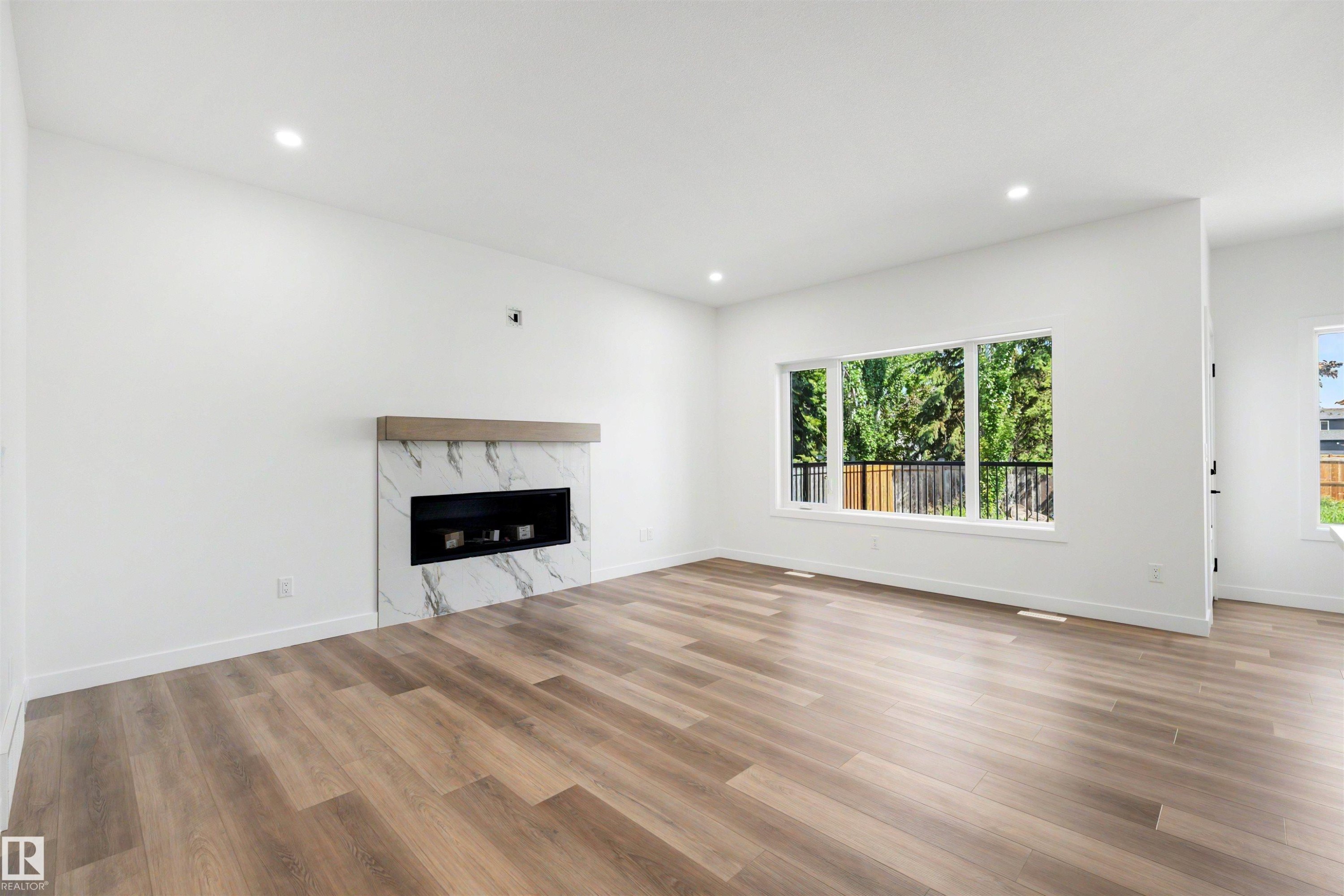 Spacious living area featuring light wood-finish flooring, recessed lighting, and a modern linear fireplace with a white marble-look surround and a wood mantel - 30 Elsinore Place Nw, Edmonton, AB