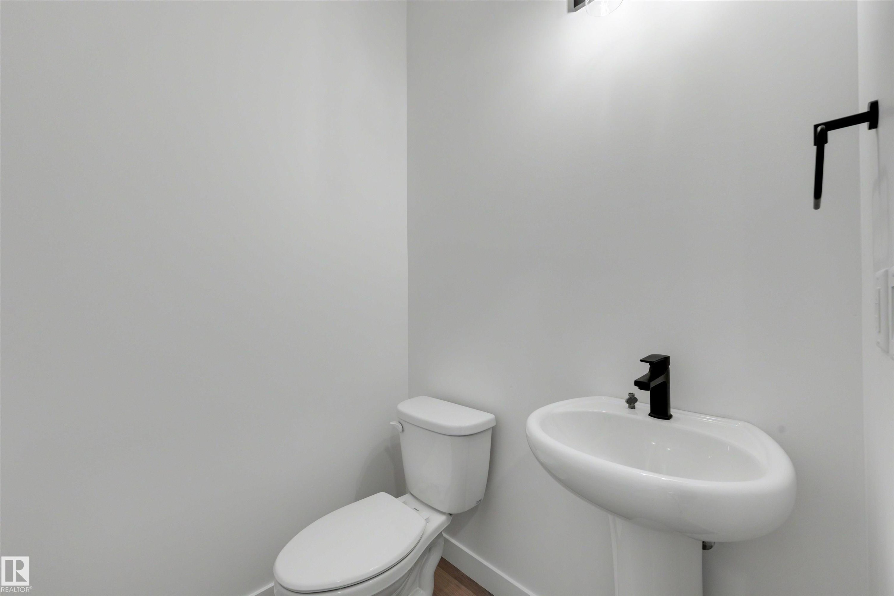 Pedestal sink with a matte black faucet, white toilet, and wood-finish flooring - 30 Elsinore Place Nw, Edmonton, AB