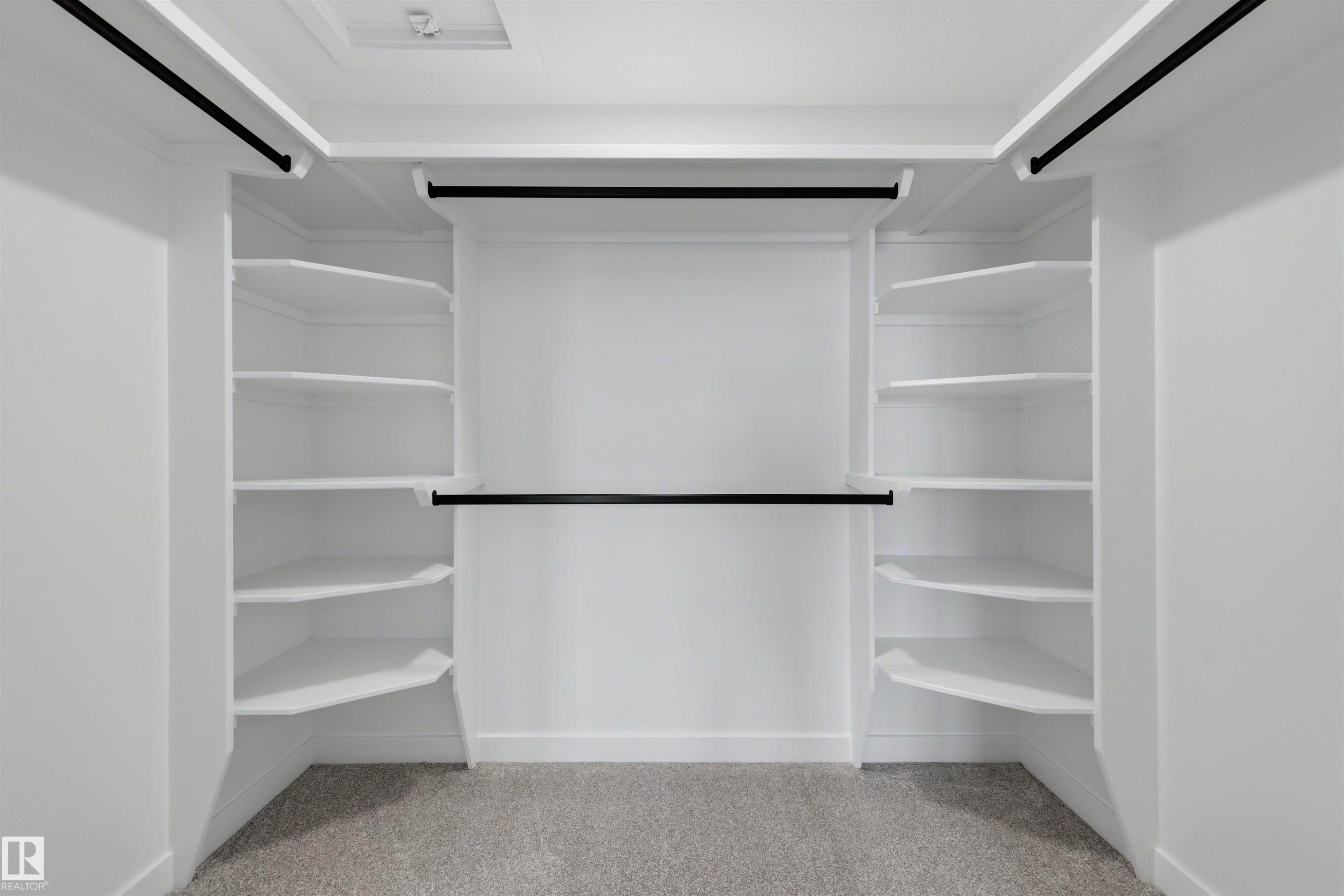 Spacious walk-in closet featuring white built-in shelving, multiple hanging rods, and light gray carpet flooring - 30 Elsinore Place Nw, Edmonton, AB