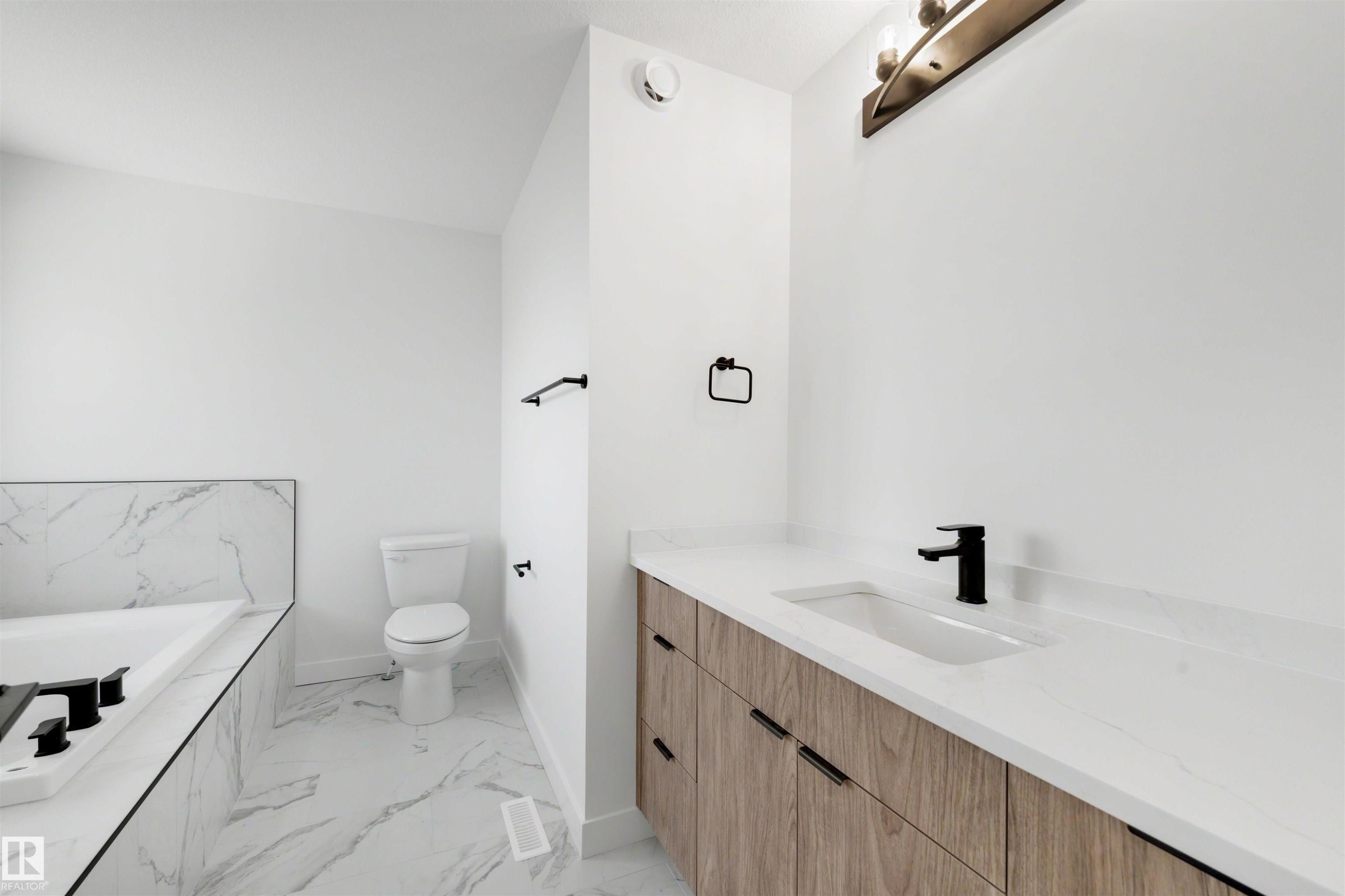 Bathroom featuring a built-in tub with tile surround, a toilet, and a vanity with a white countertop and wood-finish cabinetry - 30 Elsinore Place Nw, Edmonton, AB