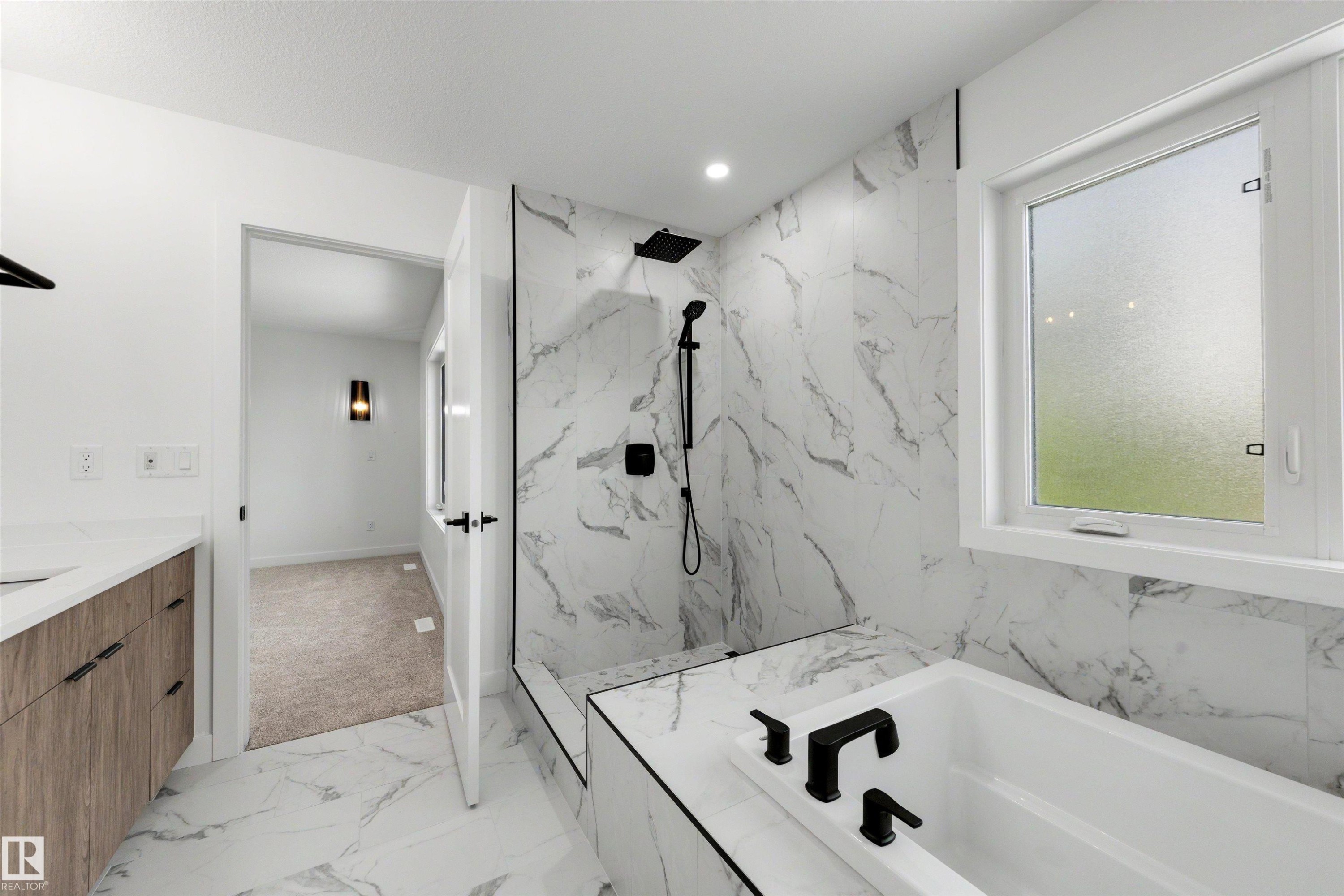Bathroom featuring large-format marble-look tile flooring, matching wall tile in the shower surround, a built-in soaking tub with matte black fixtures, and a glass-enclosed shower with a rainfall showerhead - 30 Elsinore Place Nw, Edmonton, AB