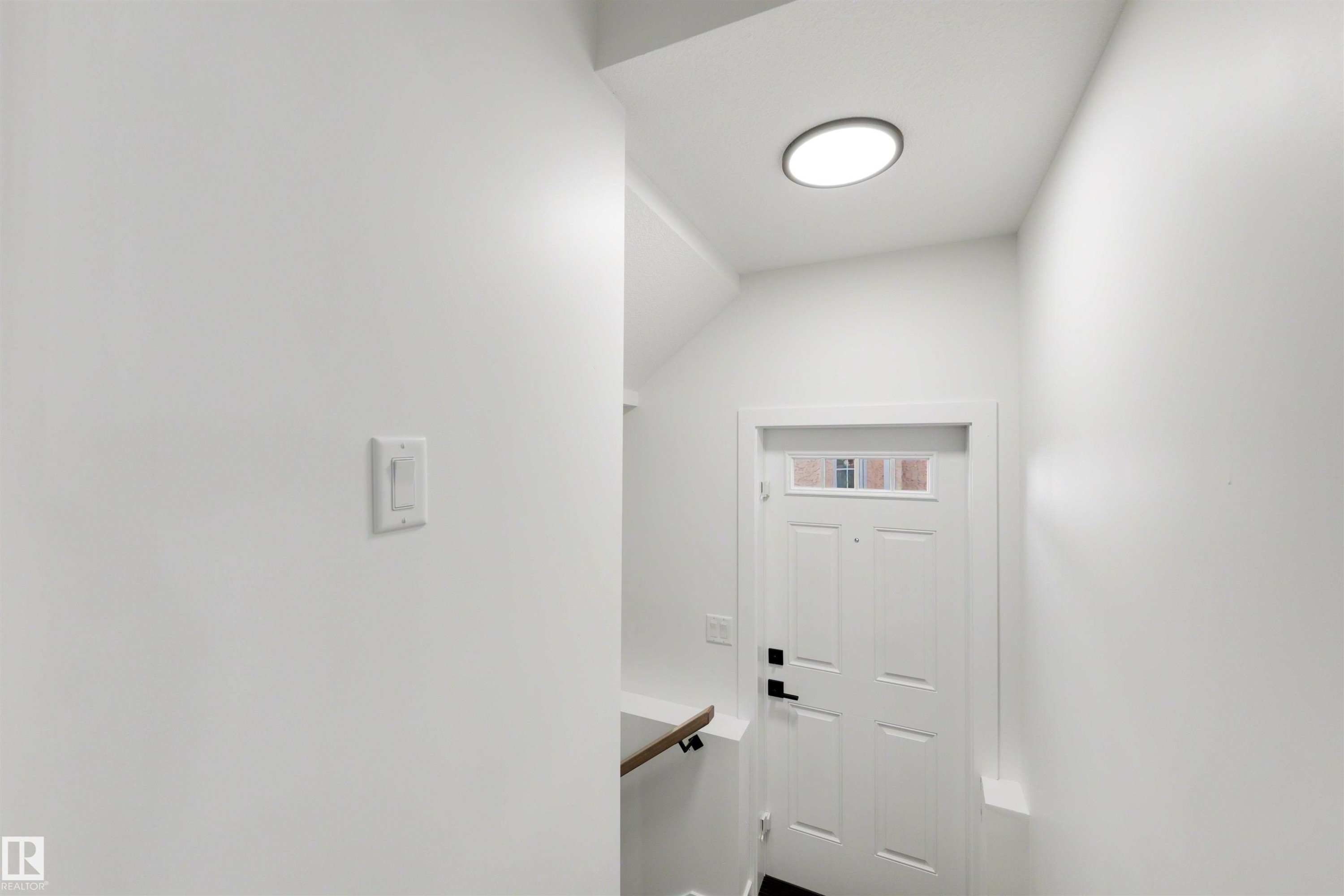 Entryway featuring a white paneled door with glass transom, black hardware, and a circular flush-mount ceiling light - 30 Elsinore Place Nw, Edmonton, AB