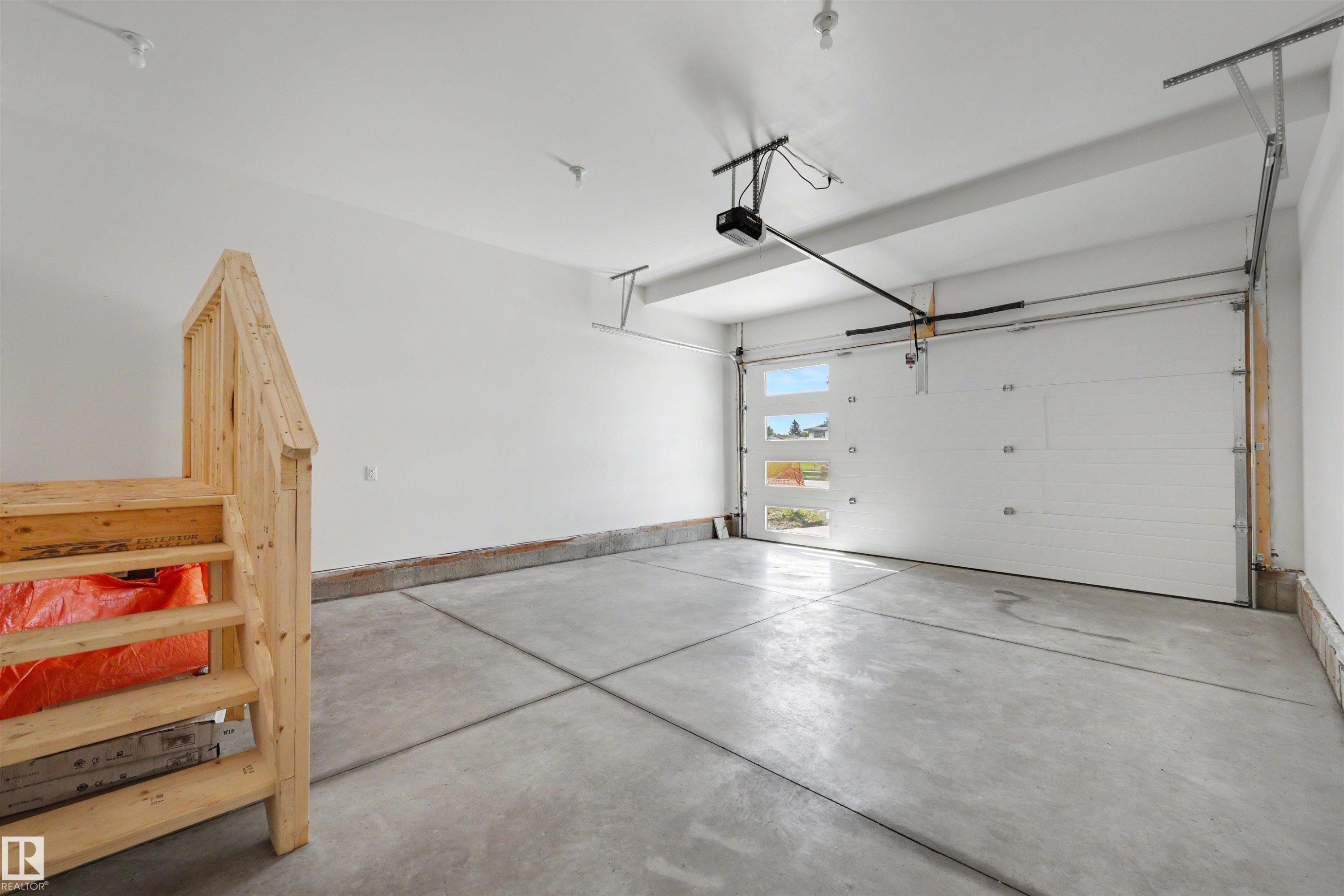 Spacious garage featuring a concrete floor, white walls, and an automatic garage door with frosted windows - 30 Elsinore Place Nw, Edmonton, AB
