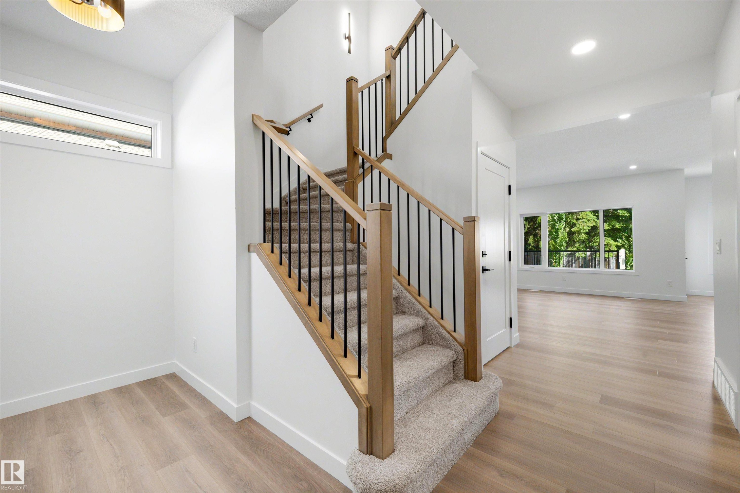 Open foyer featuring a light wood-finish staircase with black metal balusters and carpeted treads - 30 Elsinore Place Nw, Edmonton, AB