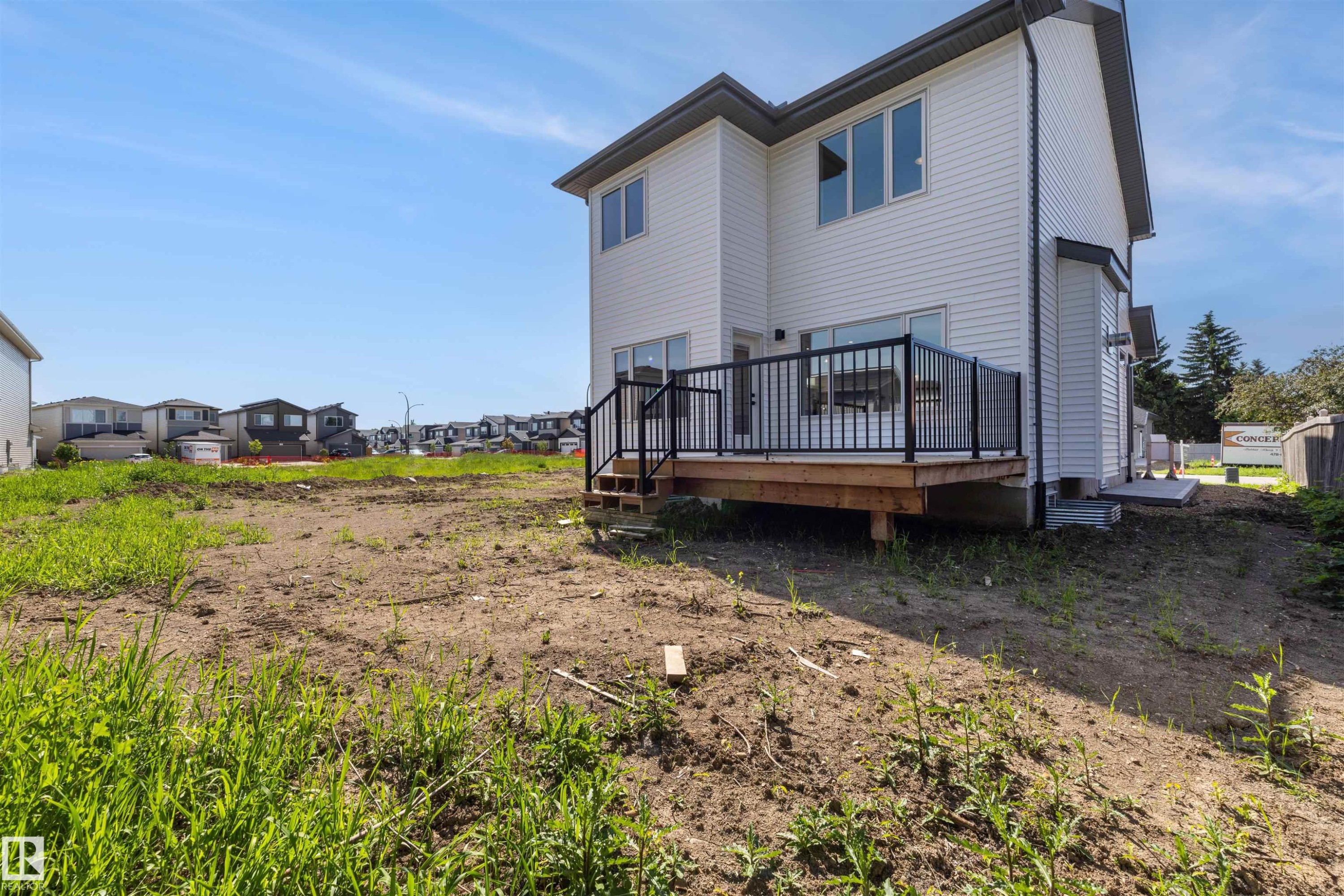 Two-story residence with white vinyl siding, a dark trim roofline, and a wooden deck featuring black railings - 30 Elsinore Place Nw, Edmonton, AB