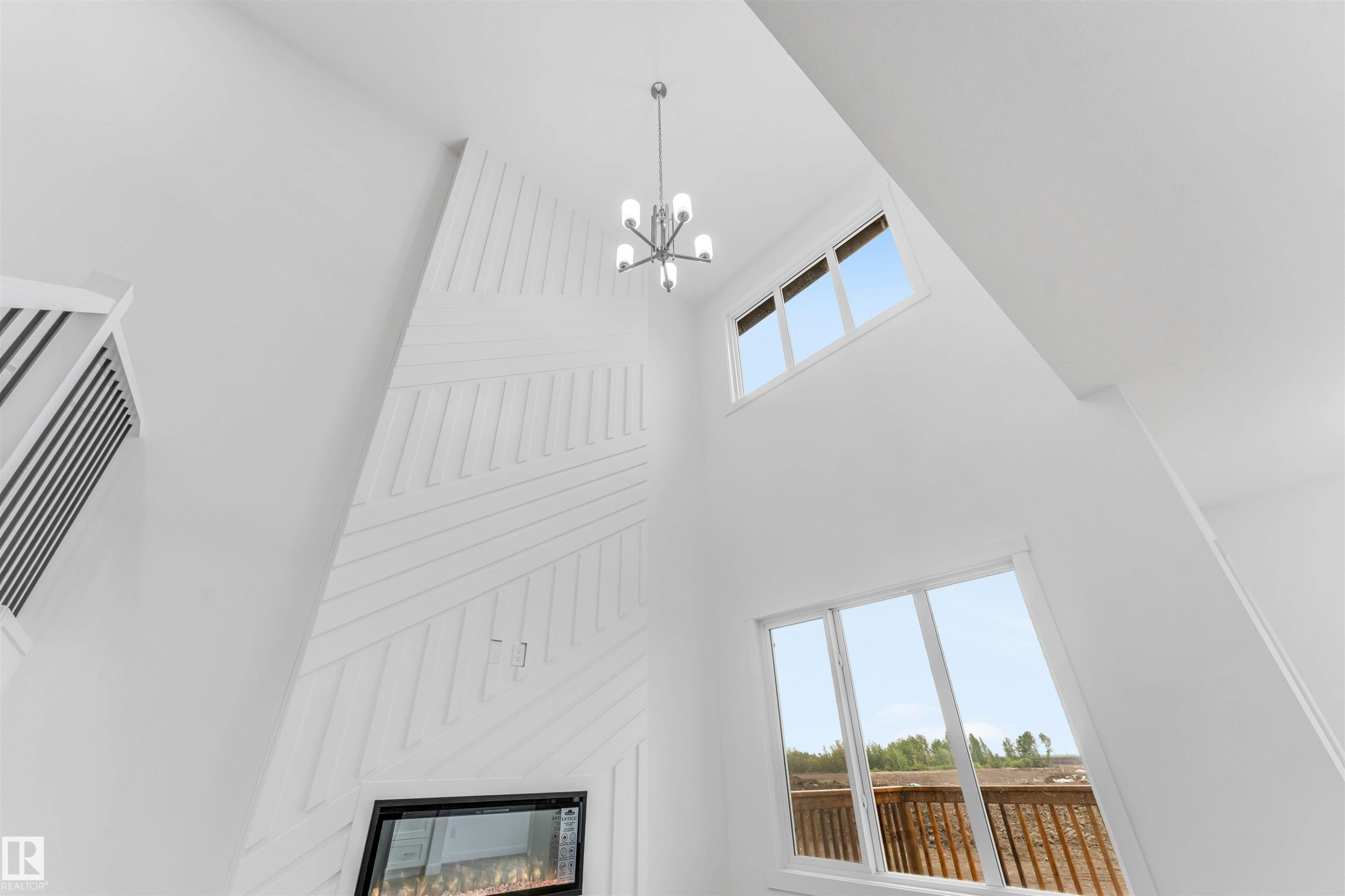 Two-story living area featuring a modern light fixture, an electric fireplace, a textured accent wall, and multiple windows - 1972 210 Street, Edmonton, AB