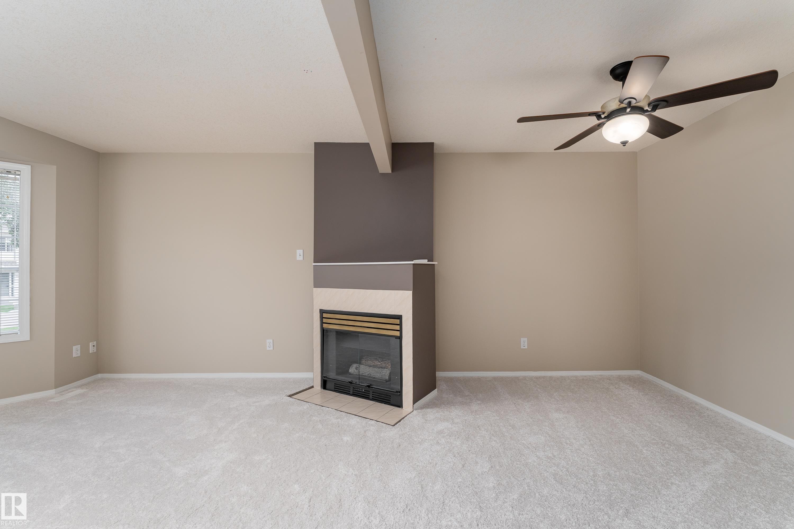 Living room featuring a fireplace with a dark accent wall, light-toned carpeting, and a ceiling fan with integrated lighting - 3 9703 174 Street, Edmonton, AB