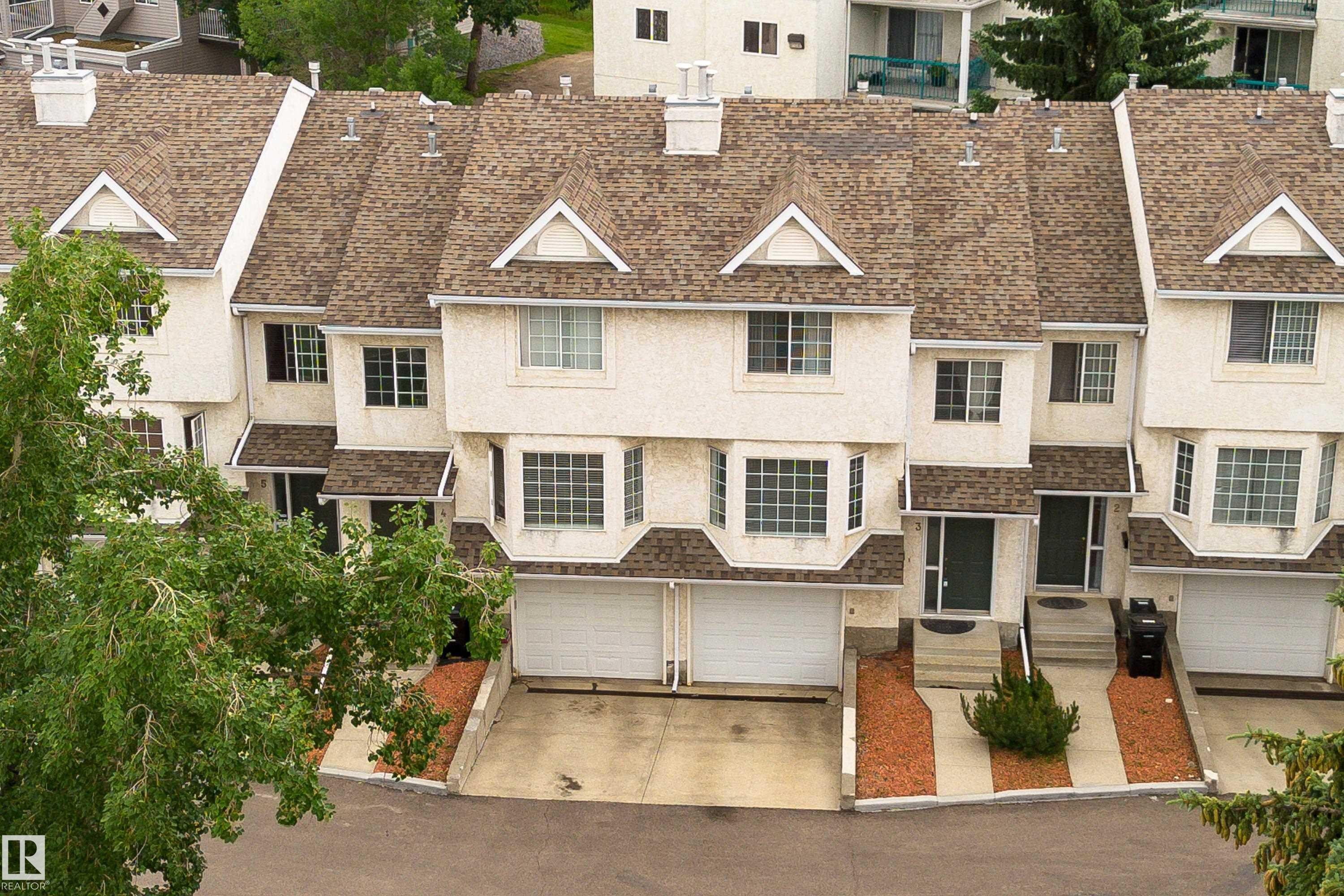 Townhome exterior featuring multiple bay windows, individual garages, and a neutral stucco finish - 3 9703 174 Street, Edmonton, AB