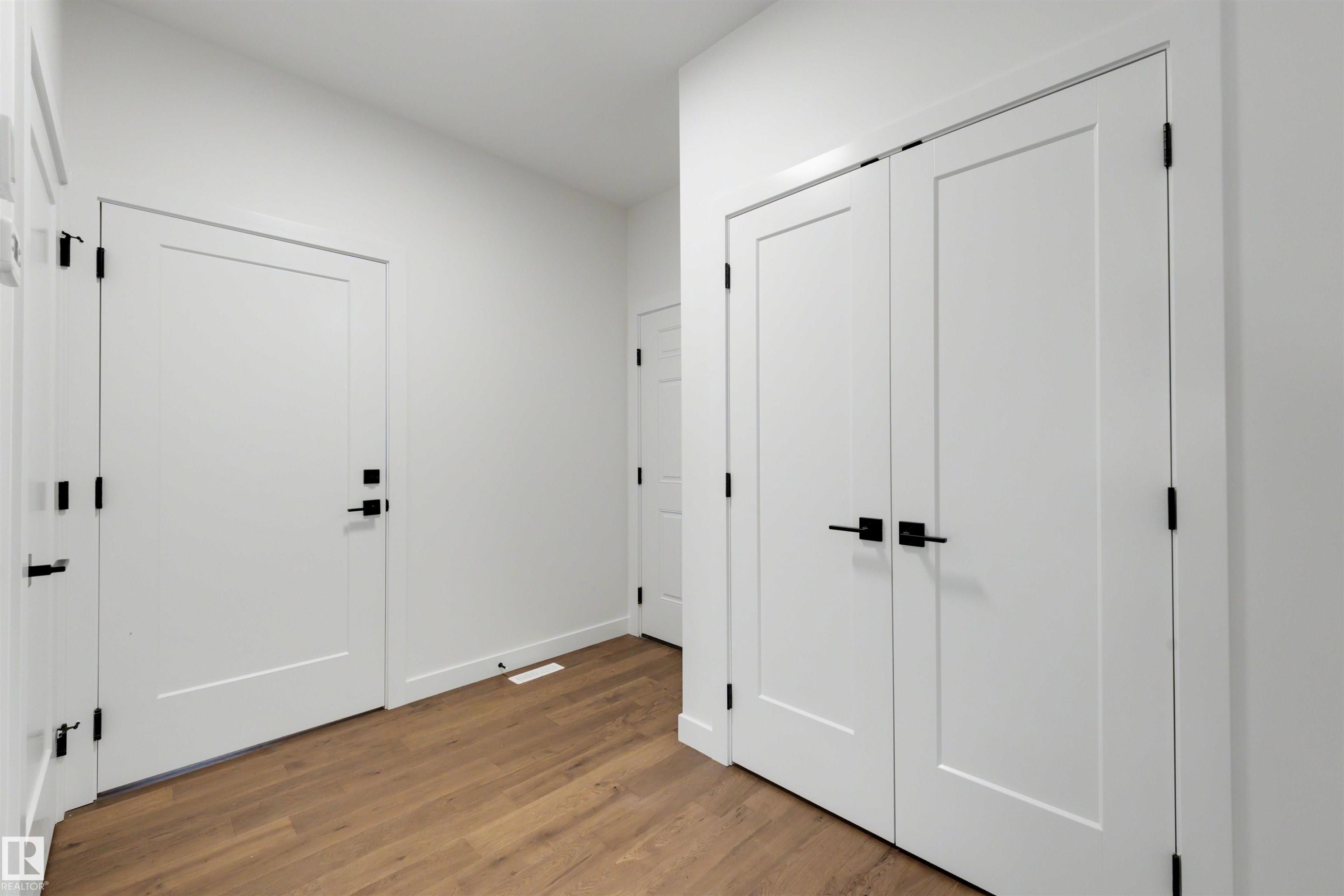 Entryway featuring wood-finish flooring, white walls, and flat-panel doors with matte black hardware - 39 Elsinore Place, Edmonton, AB