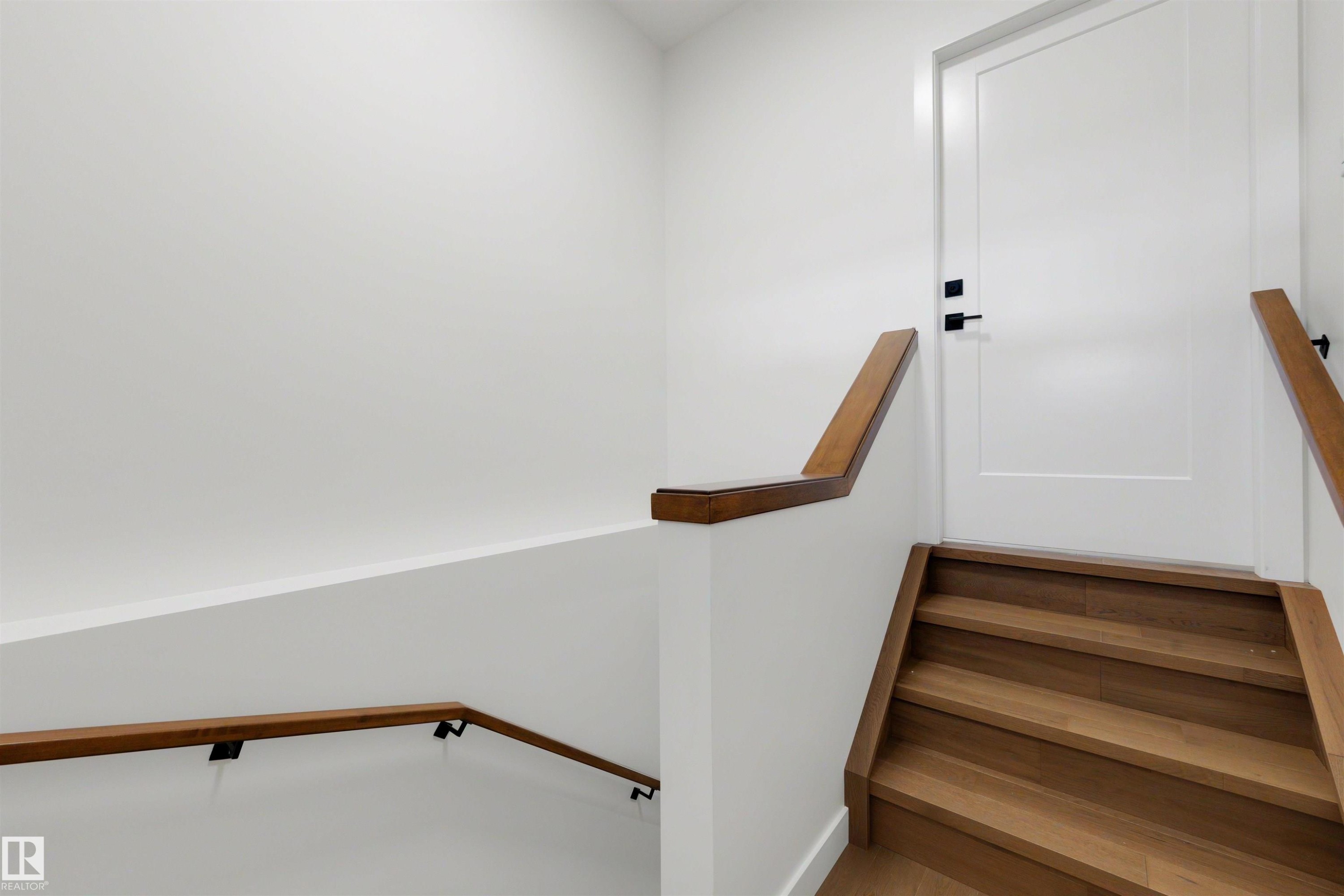 Staircase featuring wood-finish treads and risers, complemented by a solid wood handrail with matte black brackets - 39 Elsinore Place, Edmonton, AB