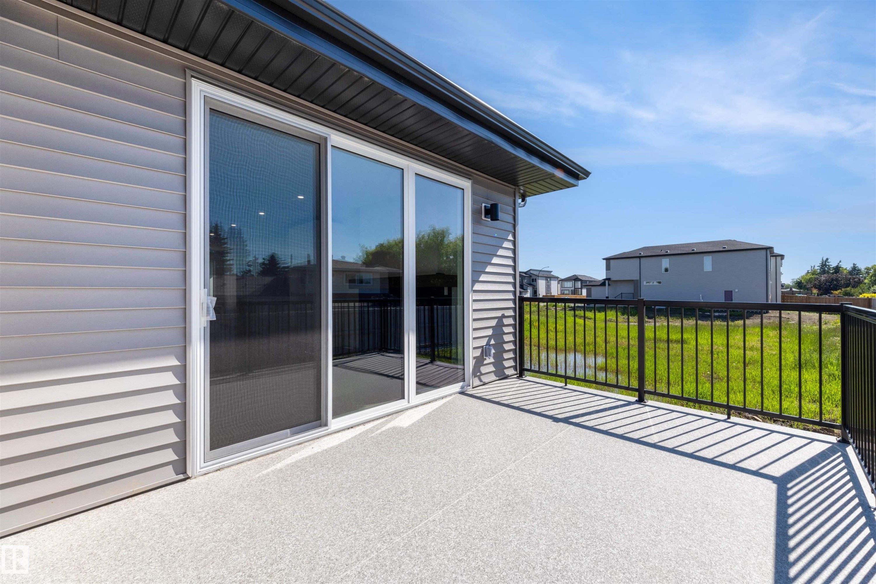 Outdoor balcony featuring a textured gray surface, black metal railings, and sliding glass doors with an integrated screen door - 39 Elsinore Place, Edmonton, AB