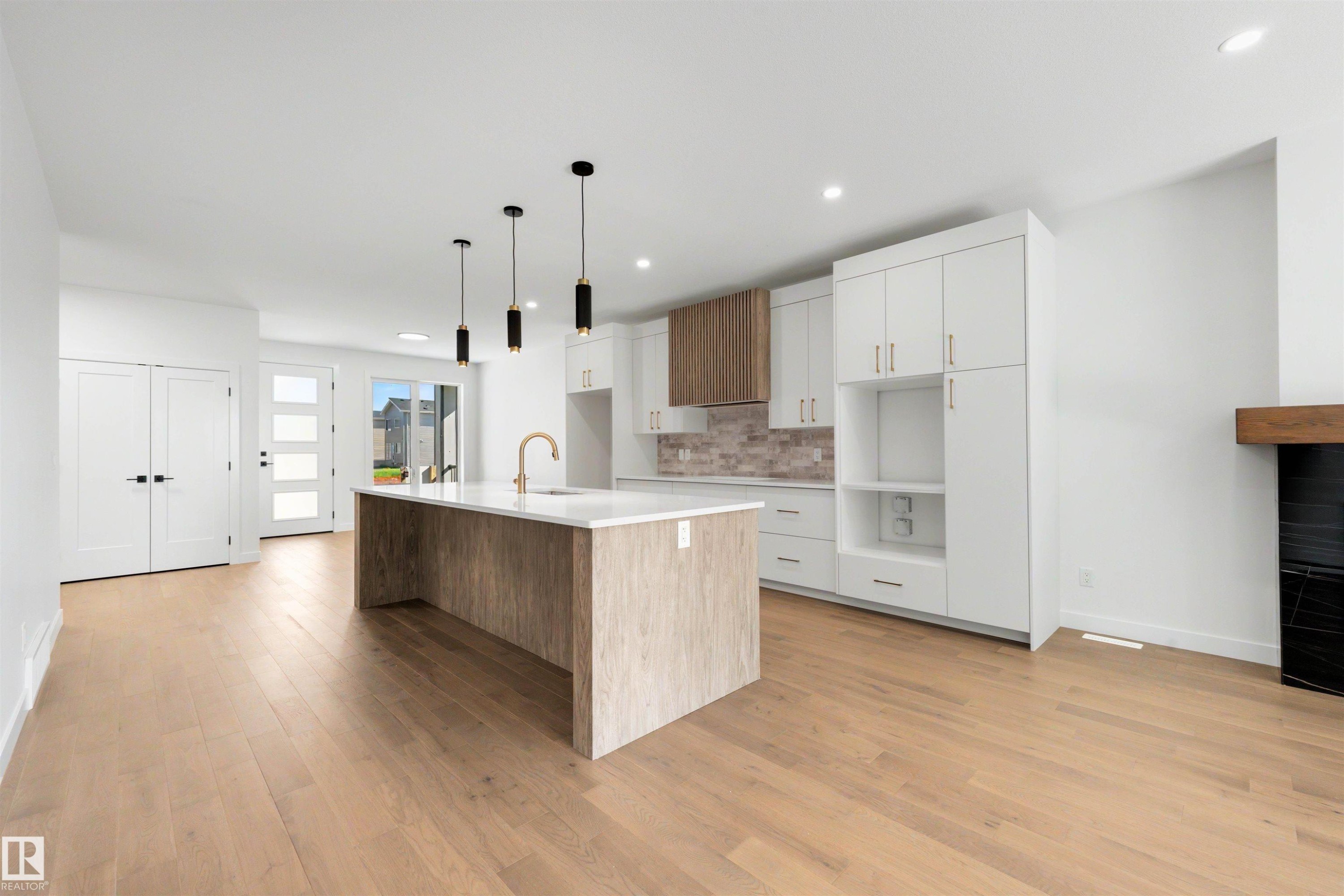 Open-concept kitchen featuring a large island with white countertop, brass faucet, and three pendant lights - 39 Elsinore Place, Edmonton, AB