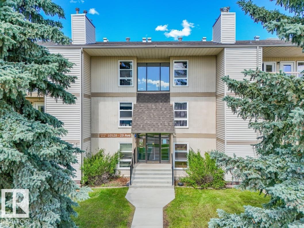 Multi-story building featuring a central entrance with a pitched roof accent, varied siding, and multiple windows - #301 10528 29 Av Nw, Edmonton, AB