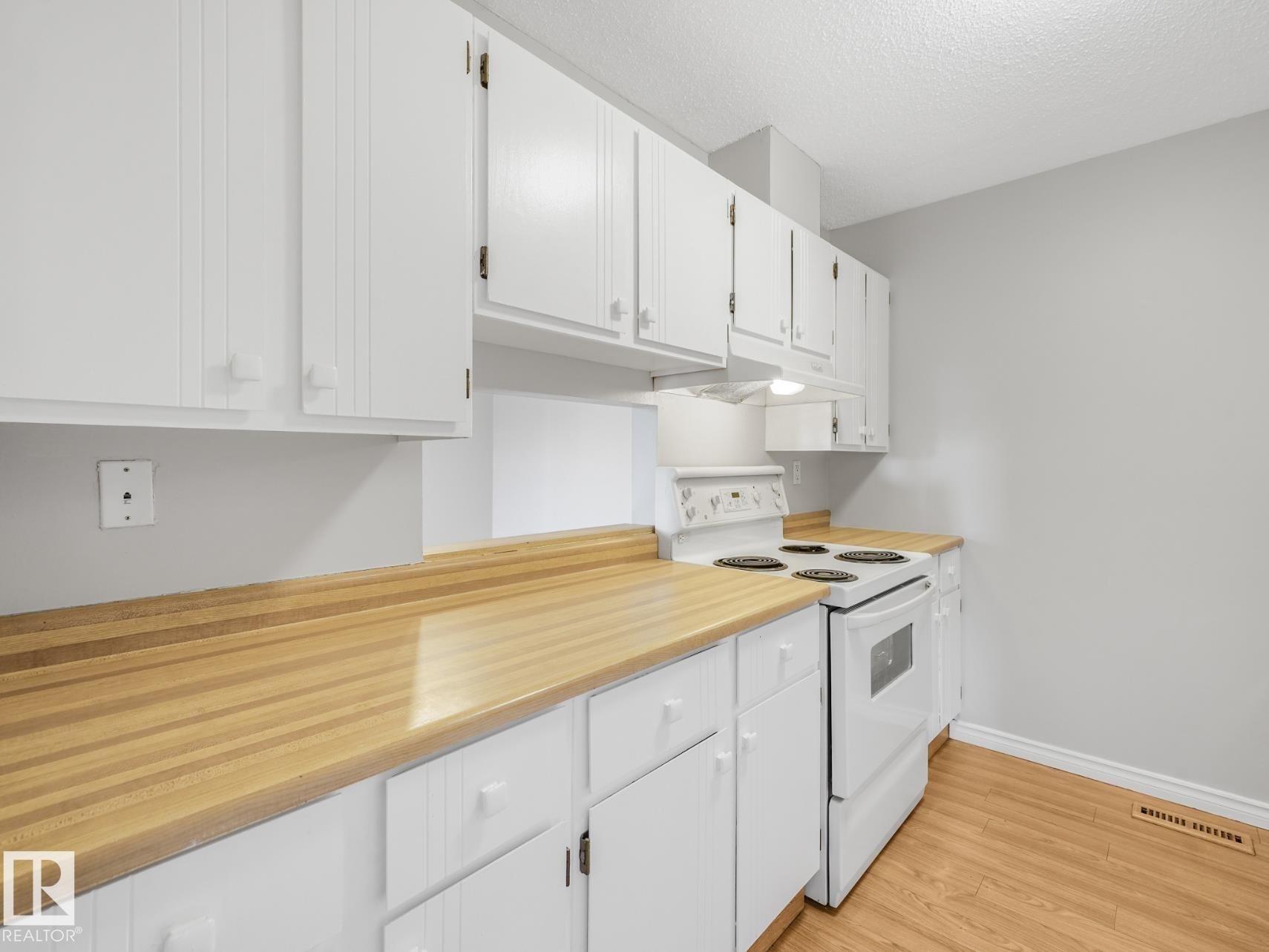 Kitchen featuring abundant white cabinetry, butcher block style countertops, a white electric range, and wood-finish flooring - #301 10528 29 Av Nw, Edmonton, AB