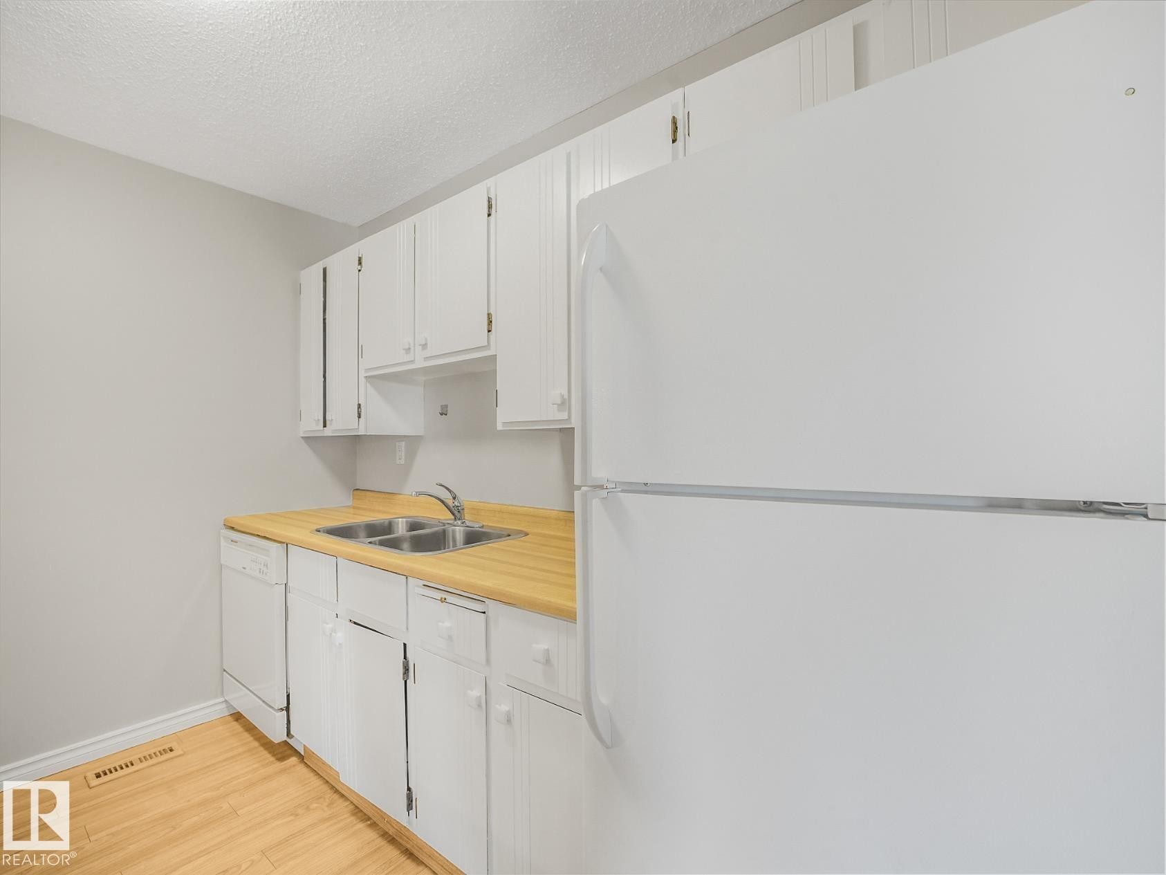 Kitchen featuring white cabinetry, wood-finish countertops, and a double basin stainless steel sink - #301 10528 29 Av Nw, Edmonton, AB