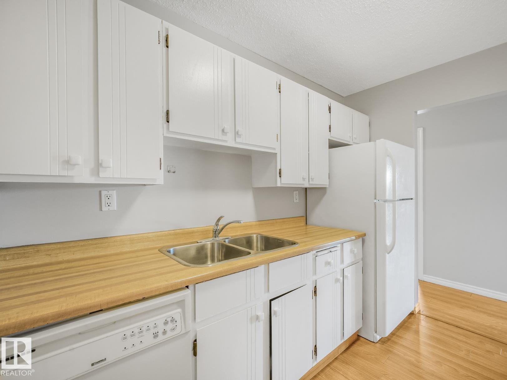 Kitchen featuring white cabinetry, wood-finish countertops, and a double-basin stainless steel sink with a chrome faucet - #301 10528 29 Av Nw, Edmonton, AB