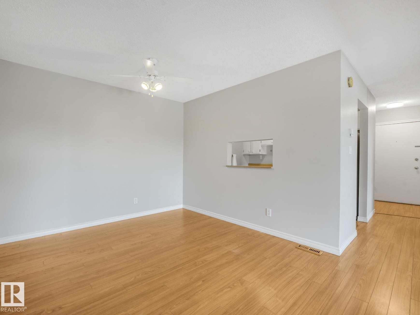 Spacious living area featuring light wood-finish flooring, light grey painted walls, white baseboards, and a ceiling fan with integrated lighting - #301 10528 29 Av Nw, Edmonton, AB