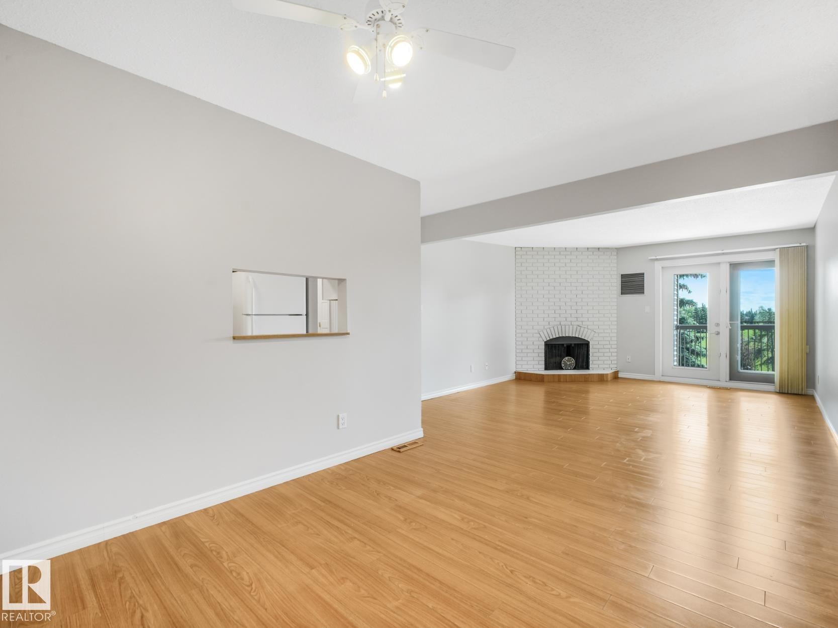 Bright interior showcasing wood-finish flooring, a white brick fireplace, and double glass doors - #301 10528 29 Av Nw, Edmonton, AB