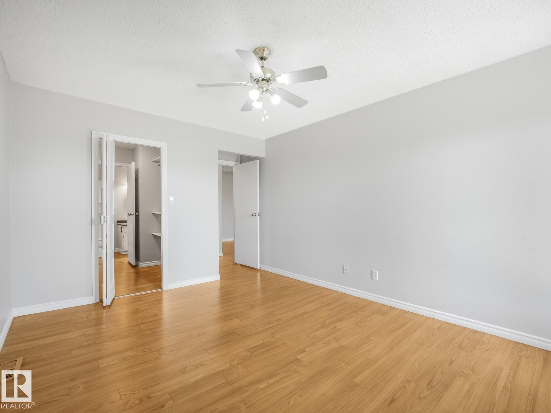 Spacious room featuring wood-finish flooring, light gray walls, and a ceiling fan with integrated lighting - #301 10528 29 Av Nw, Edmonton, AB