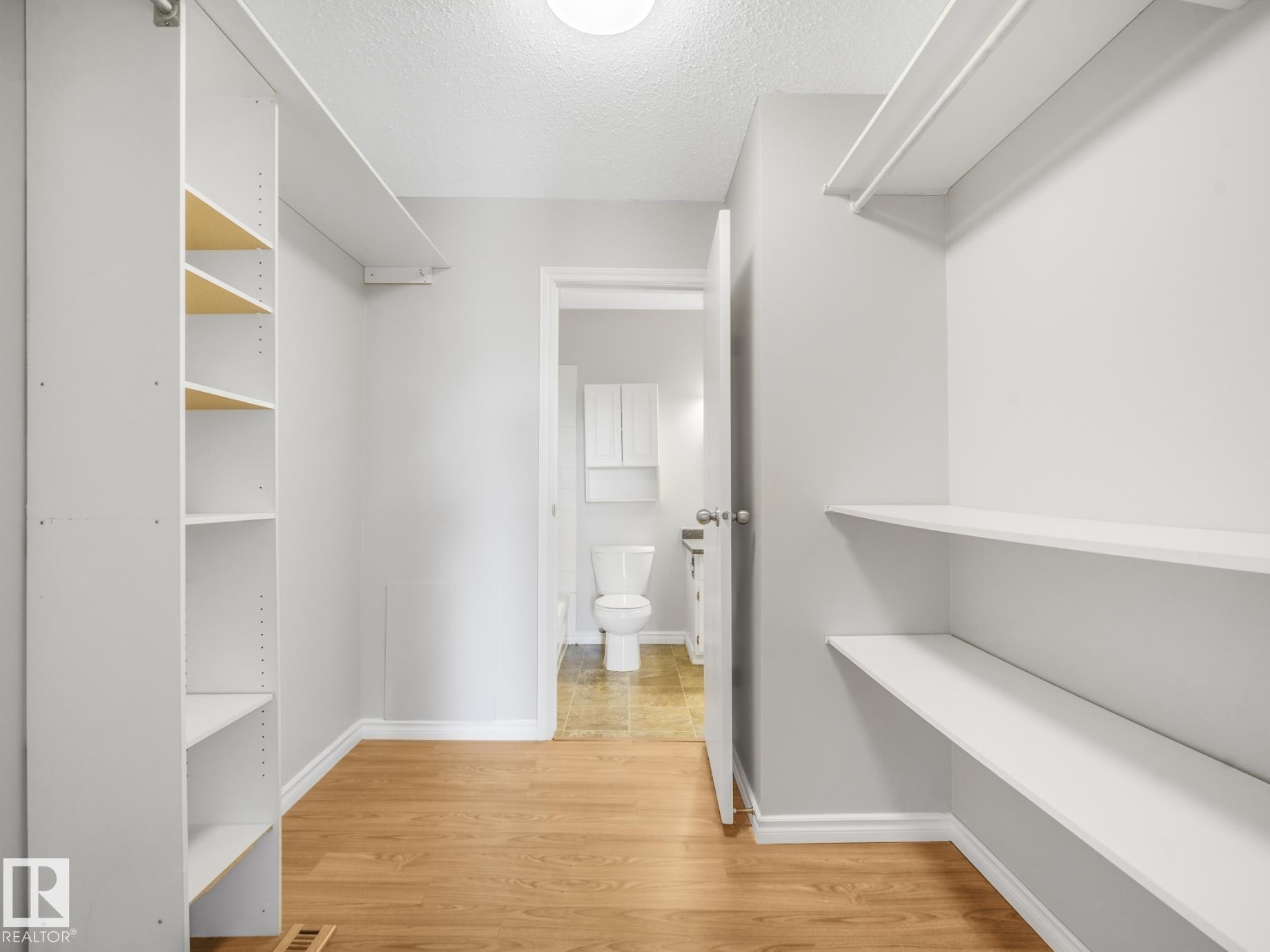 Walk-in closet featuring wood-finish flooring, white shelving units, and a bright overhead light fixture - #301 10528 29 Av Nw, Edmonton, AB