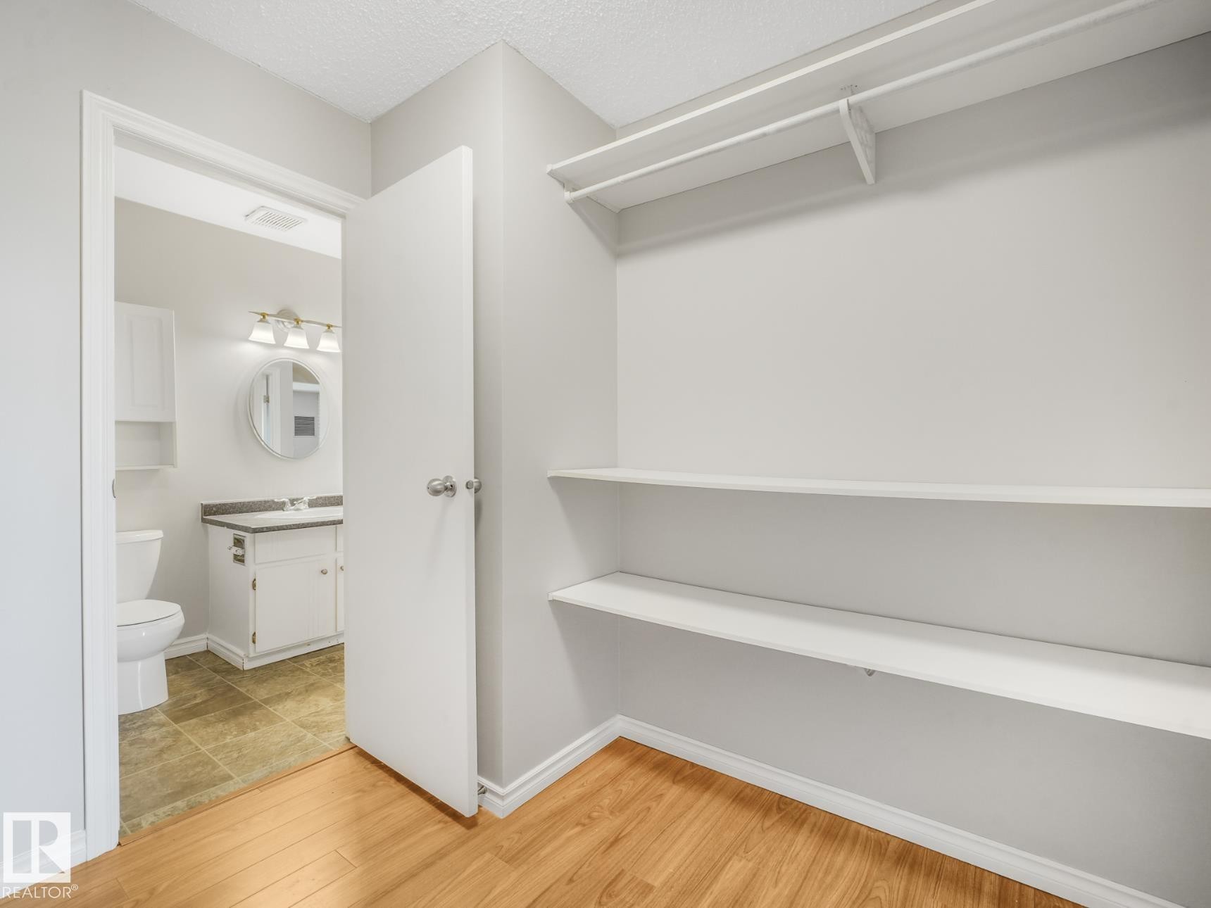 Hardwood-finish flooring extending into a spacious closet with built-in shelving and hanging rod - #301 10528 29 Av Nw, Edmonton, AB