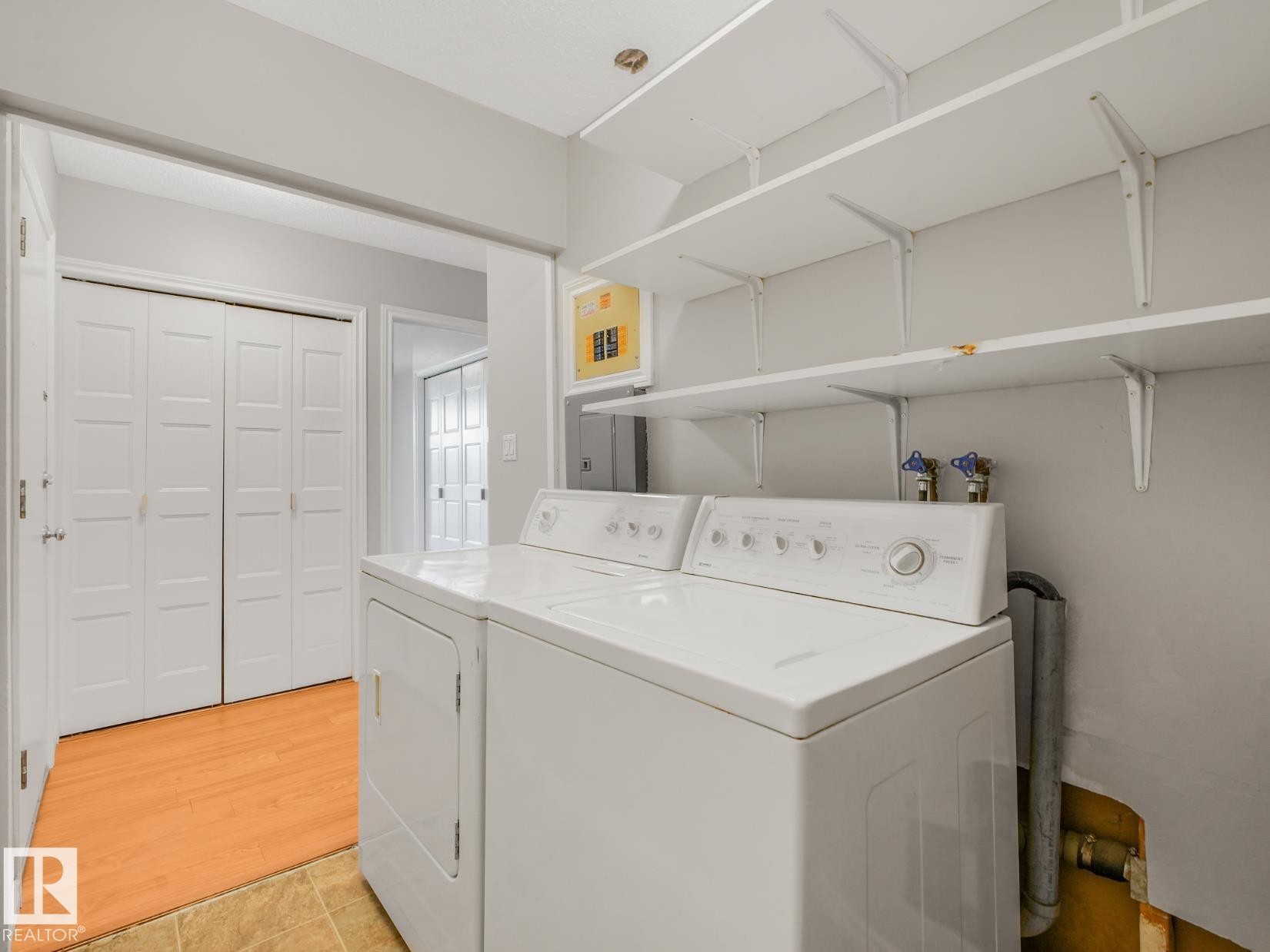 Dedicated laundry area featuring a washer and dryer, extensive wall-mounted shelving, and paneled bifold closet doors - #301 10528 29 Av Nw, Edmonton, AB