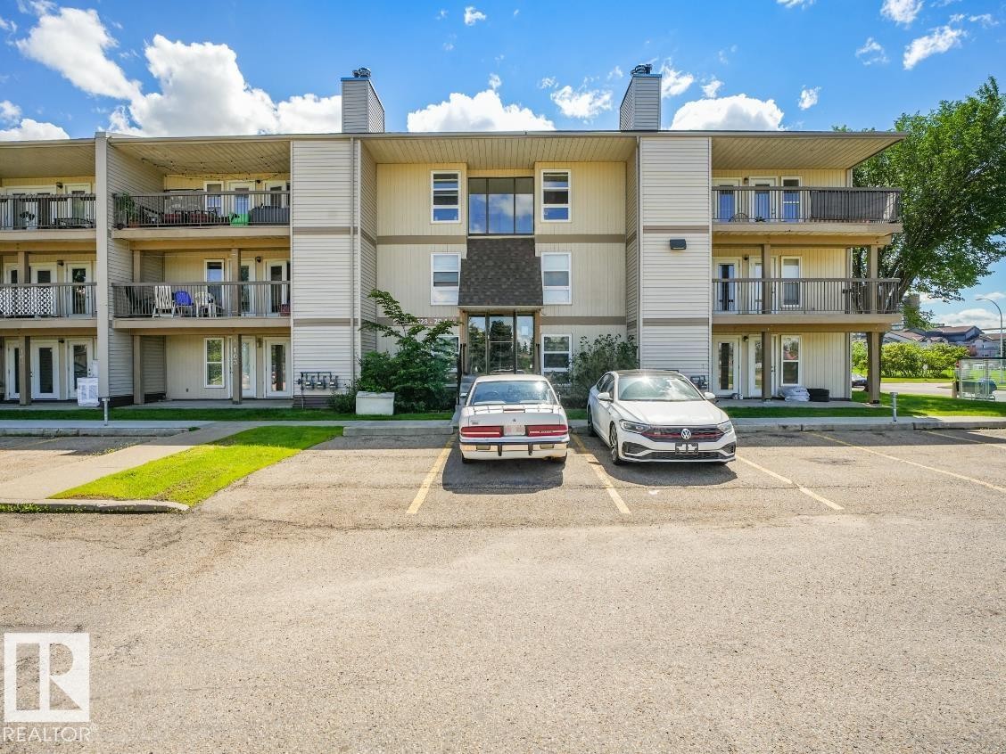 Multi-story residential building featuring balconies with black railings, tan siding, and a gabled entrance - #301 10528 29 Av Nw, Edmonton, AB