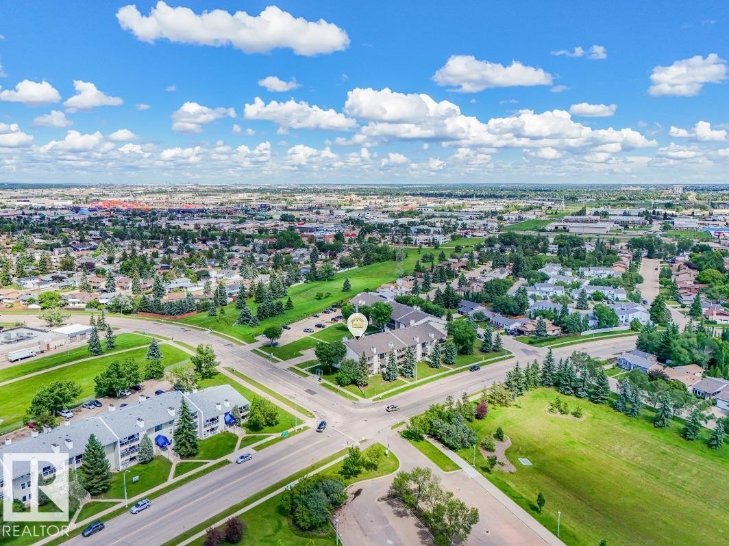 Aerial perspective showcasing a multi-story residential building with light-colored siding and a dark roof, surrounded by mature trees and manicured green spaces - #301 10528 29 Av Nw, Edmonton, AB