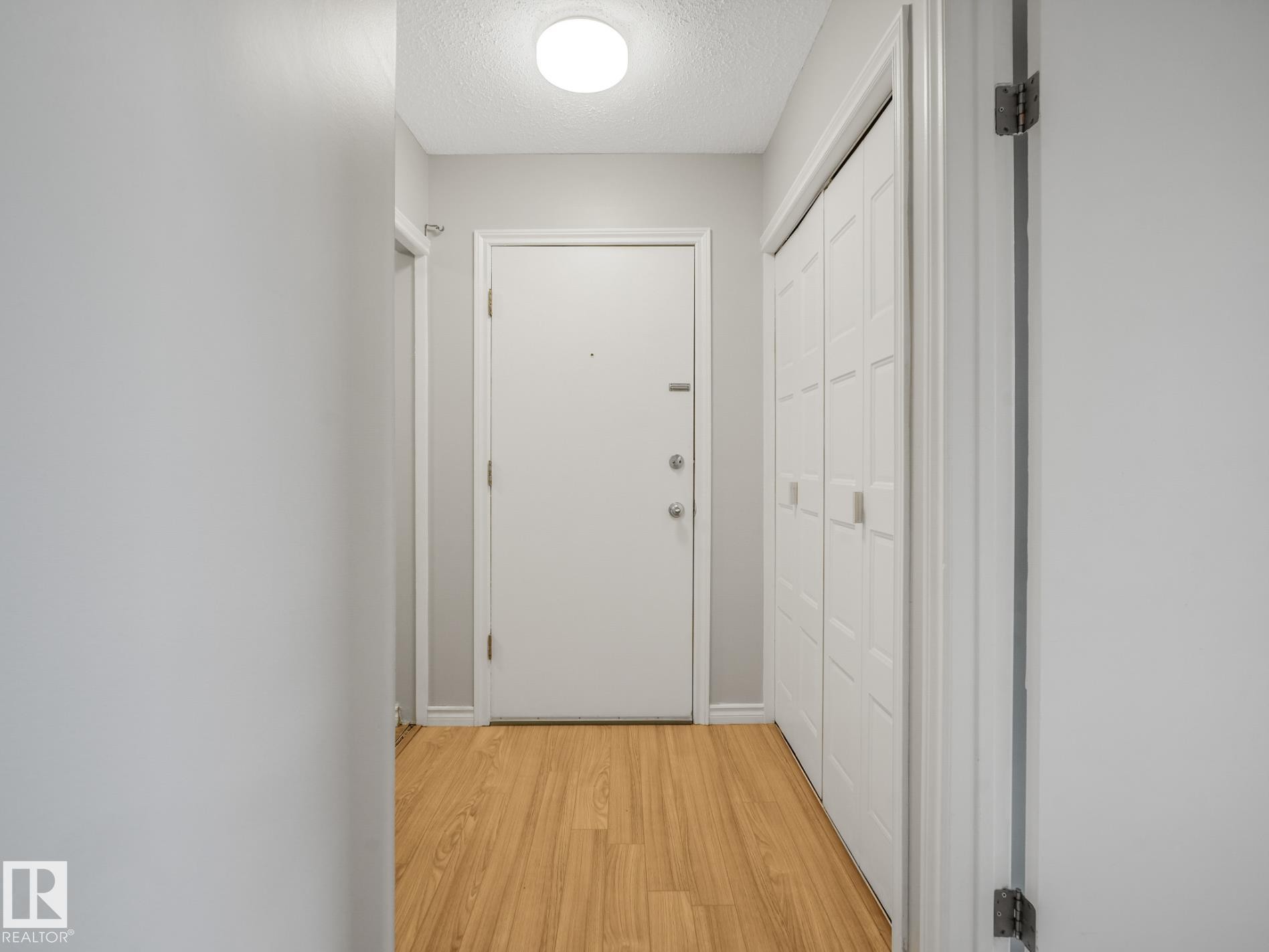Entryway featuring wood-finish flooring, a flush-mount ceiling light, white paneled doors, and bi-fold closet doors - #301 10528 29 Av Nw, Edmonton, AB