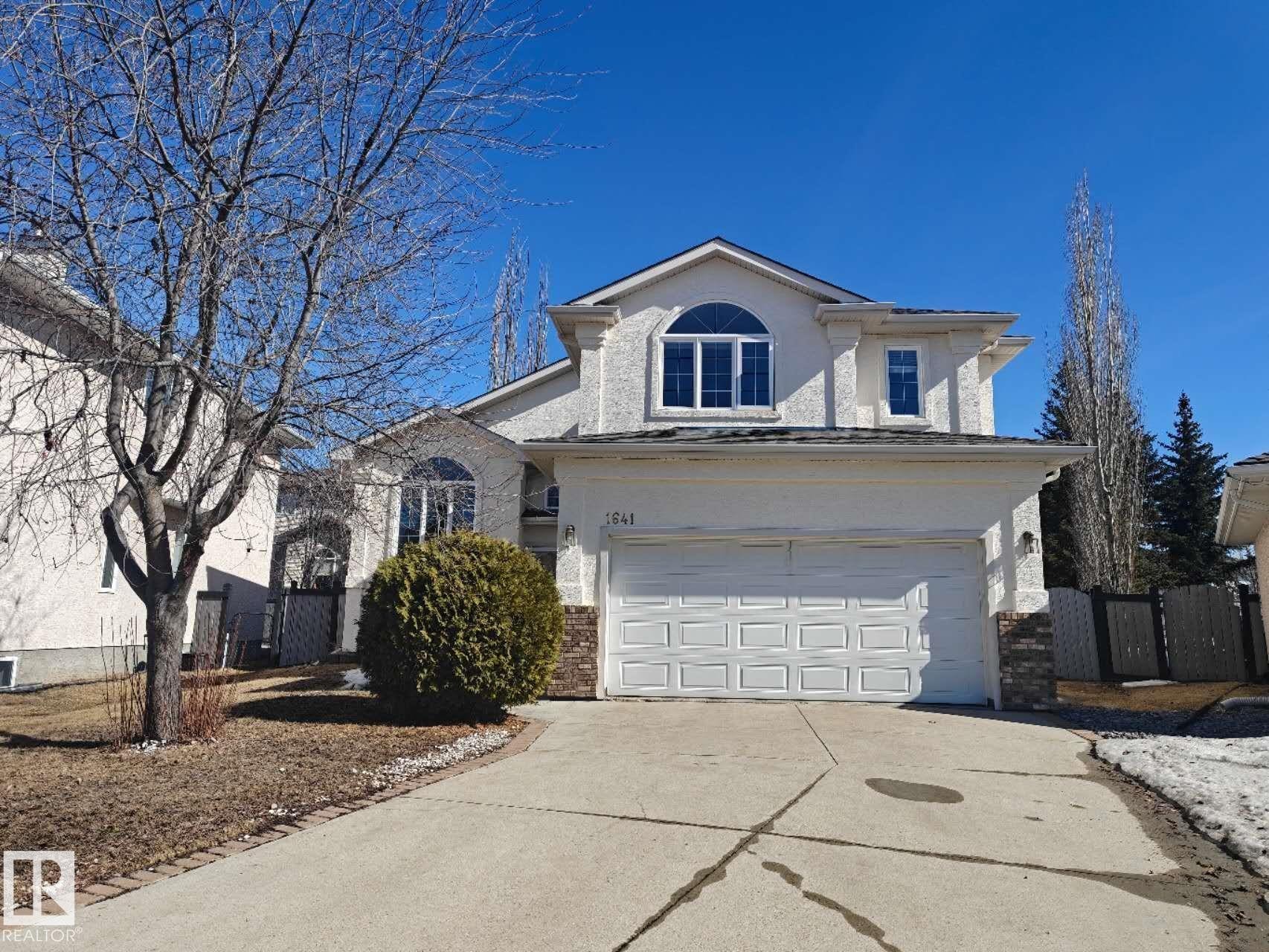 Two-story stucco residence featuring an attached double garage, an arched window, and a concrete driveway - 1641 Forbes Way, Edmonton, AB - Outdoor