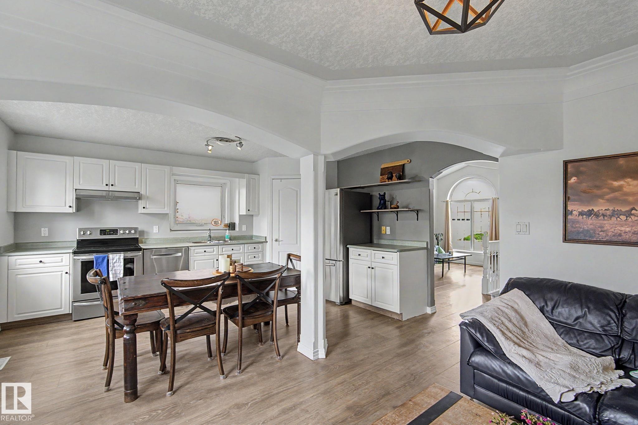 Open-concept kitchen and dining area featuring white cabinetry, stainless steel appliances, and light wood-finish flooring - 1619 Welbourn Cove, Edmonton, AB