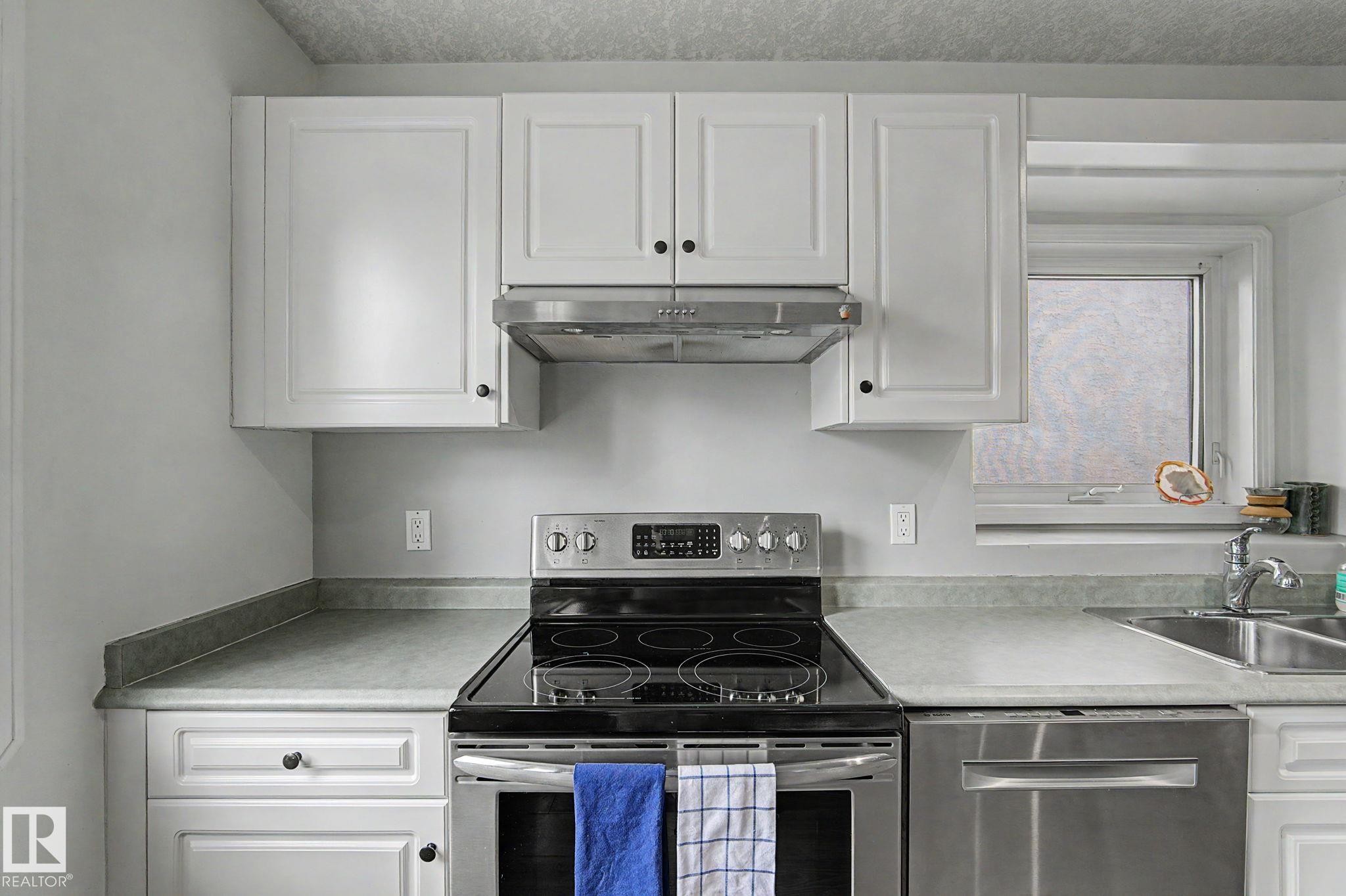 Kitchen featuring white cabinetry, stainless steel appliances, a double basin sink, and a window above the sink - 1619 Welbourn Cove, Edmonton, AB