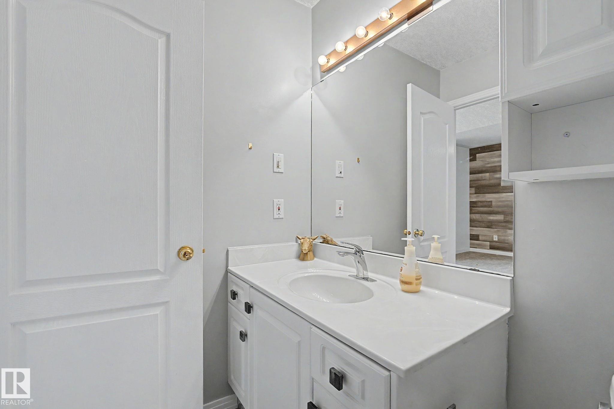 Bathroom vanity featuring a white countertop with an integrated sink, a single-handle chrome faucet, and a large mirror with overhead vanity lighting - 1619 Welbourn Cove, Edmonton, AB